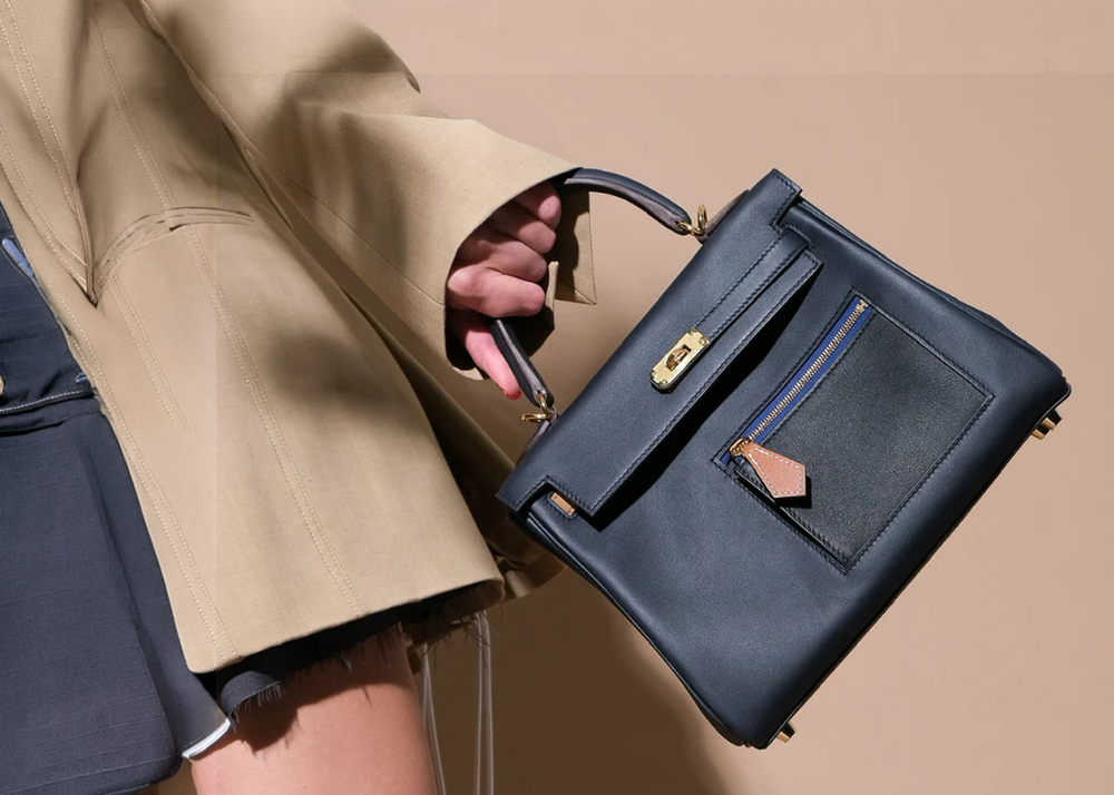 A blue Colormatic Kelly with an exterior pocket, carried with camel tailoring