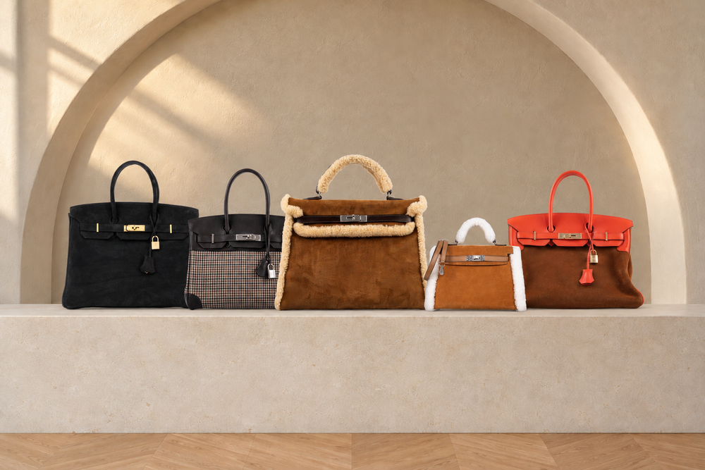 Five Hermès bags in suede, shearling and wool arranged on a limestone plinth beneath an ivory arch