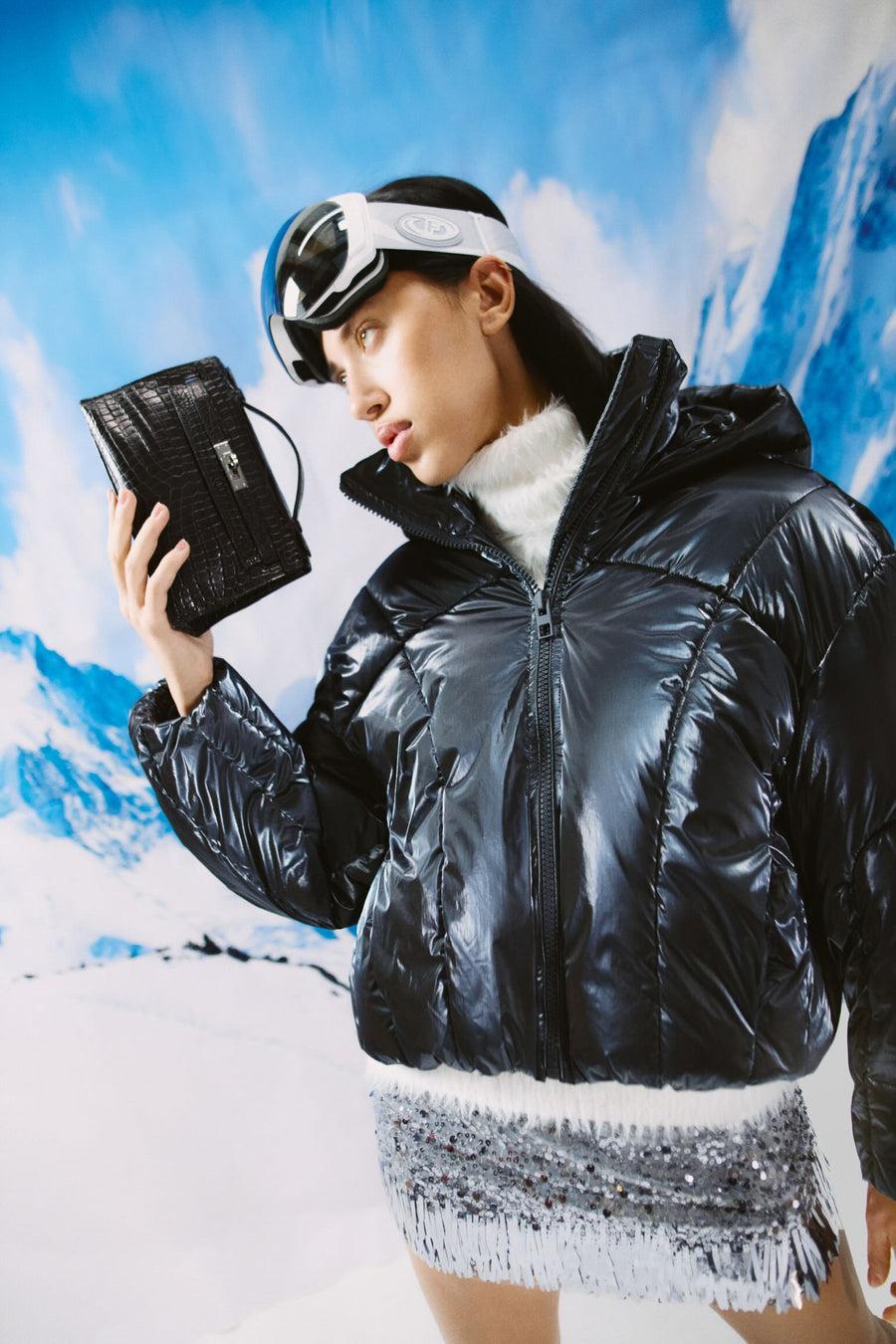 Hermès Kelly Pochette Black Alligator Gold Hardware, held up by a model in a puffer jacket
