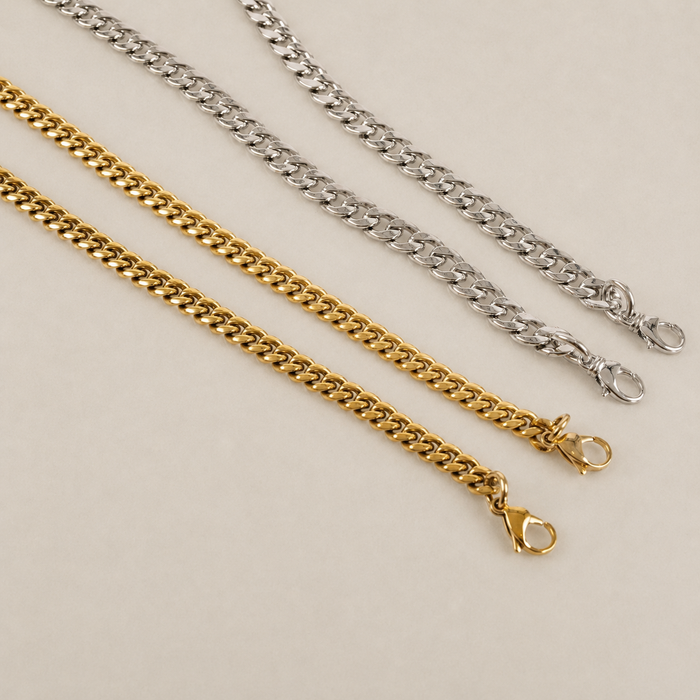 JaneFinds Cuban crossbody chains in gold and palladium finishes on a warm neutral studio background