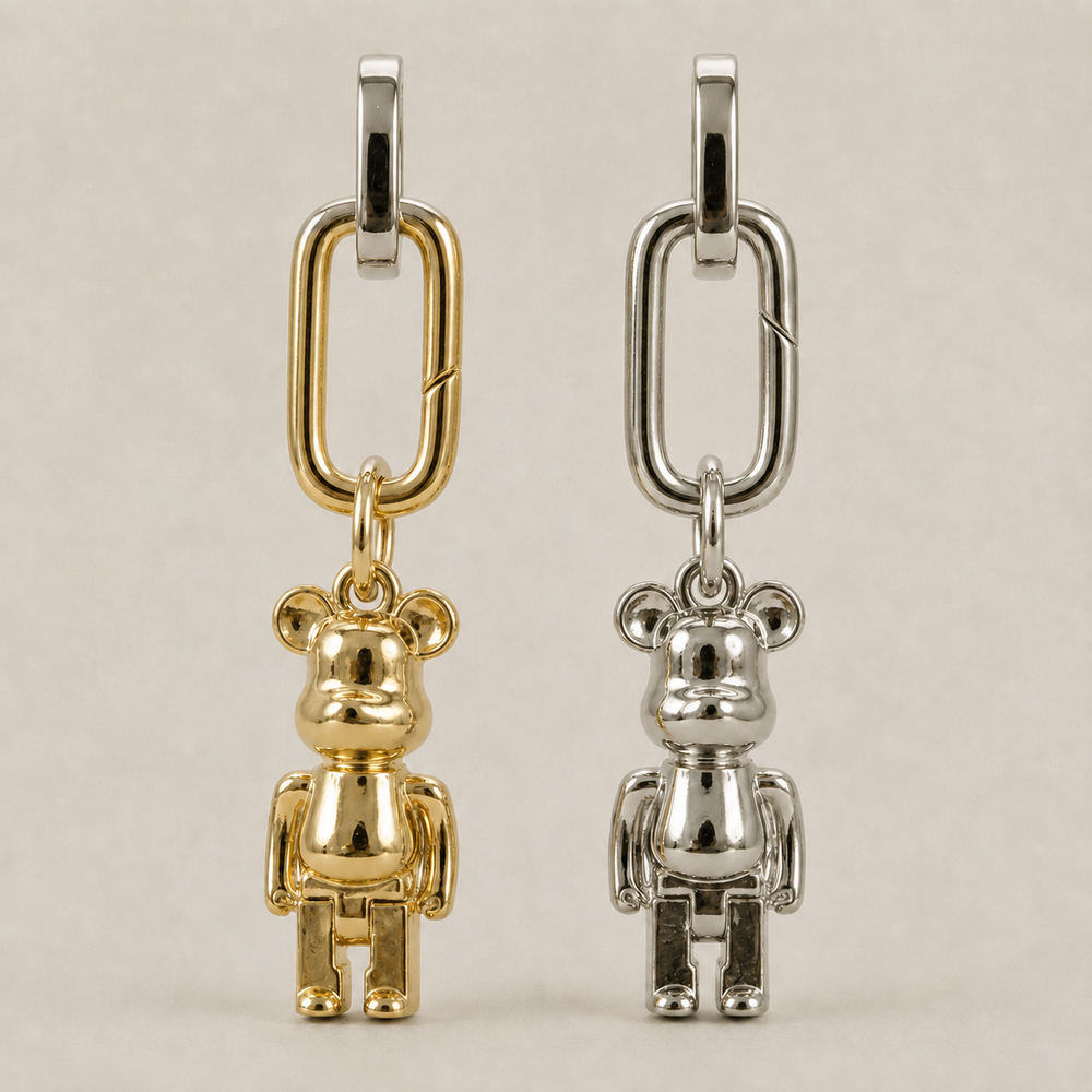 JaneFinds Lucky Bear charms in gold and palladium finishes on a warm neutral studio background