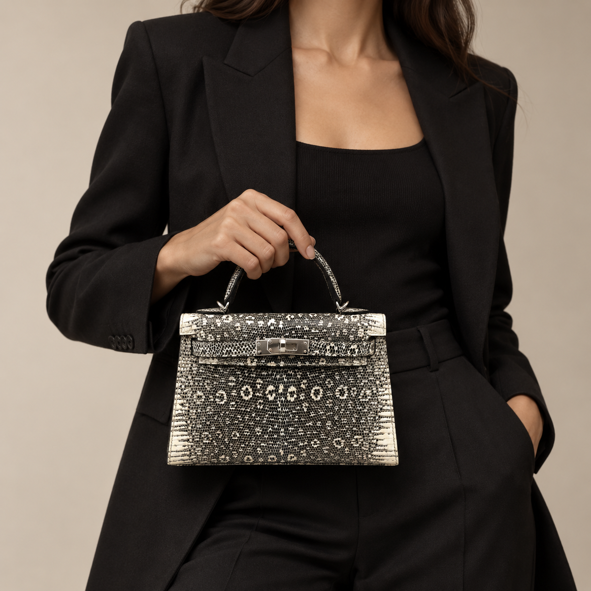 Model holding a Hermès Kelly 20 Mini II Sellier Ombré Lizard bag with palladium hardware, styled with a black tailored suit.