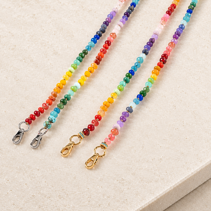 JaneFinds Rainbow semi-precious stone chains with gold and palladium clasps on pale limestone.