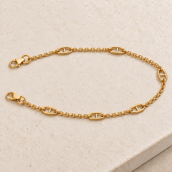 JaneFinds gold Mariner crossbody chain with anchor links, fine cable sections and claw clasps on pale limestone.