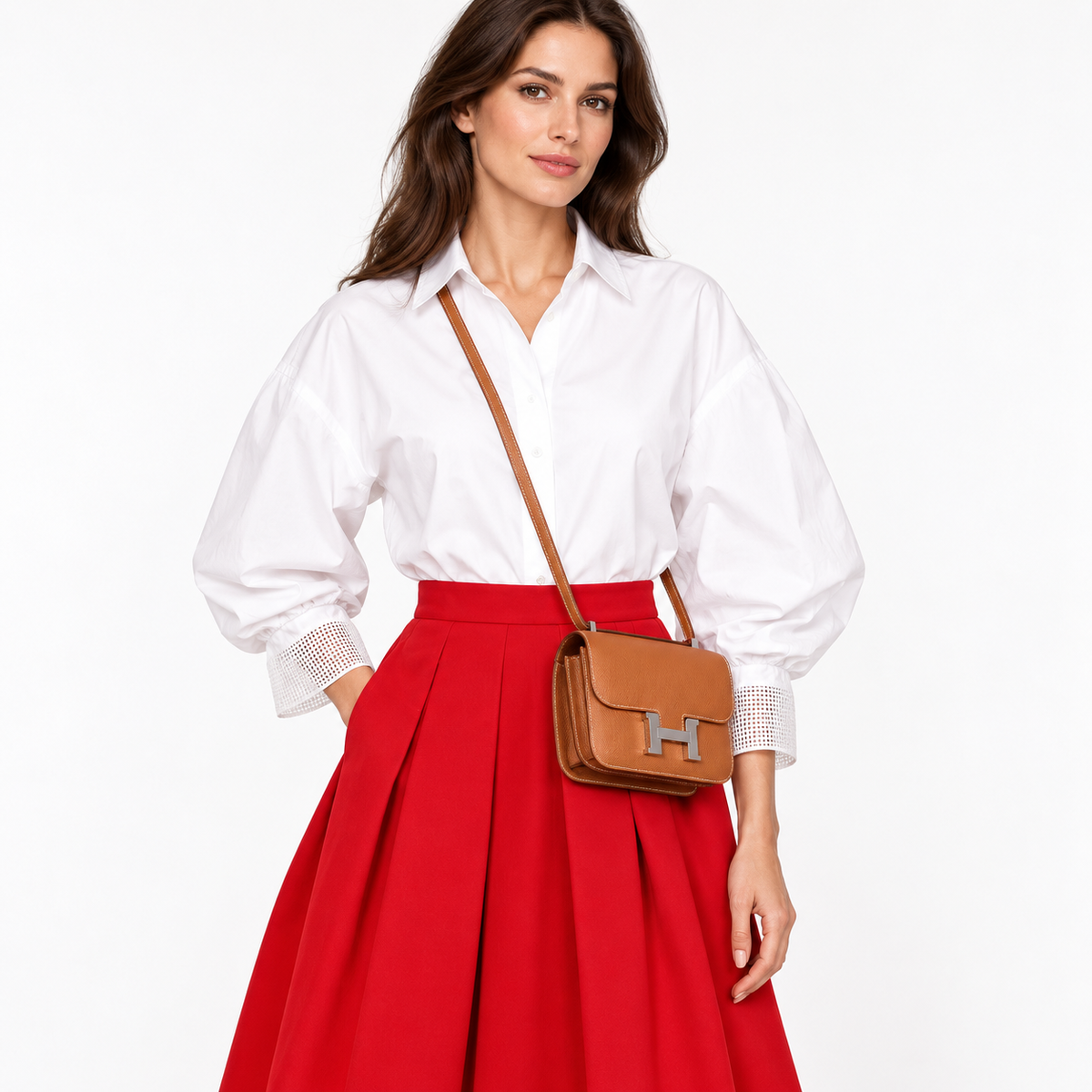 Hermès Constance 18 Mini III in Gold Epsom with palladium hardware worn crossbody by a model in a white blouse and red skirt against a clean white studio background.
