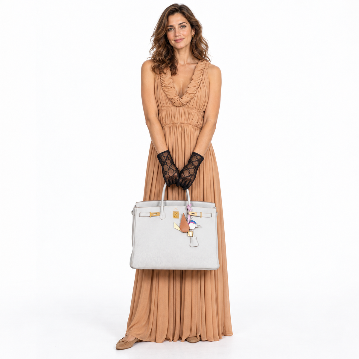 Hermès Birkin 40 Gris Perle Togo with gold hardware and bird charm carried by a woman in a peach dress in a white studio