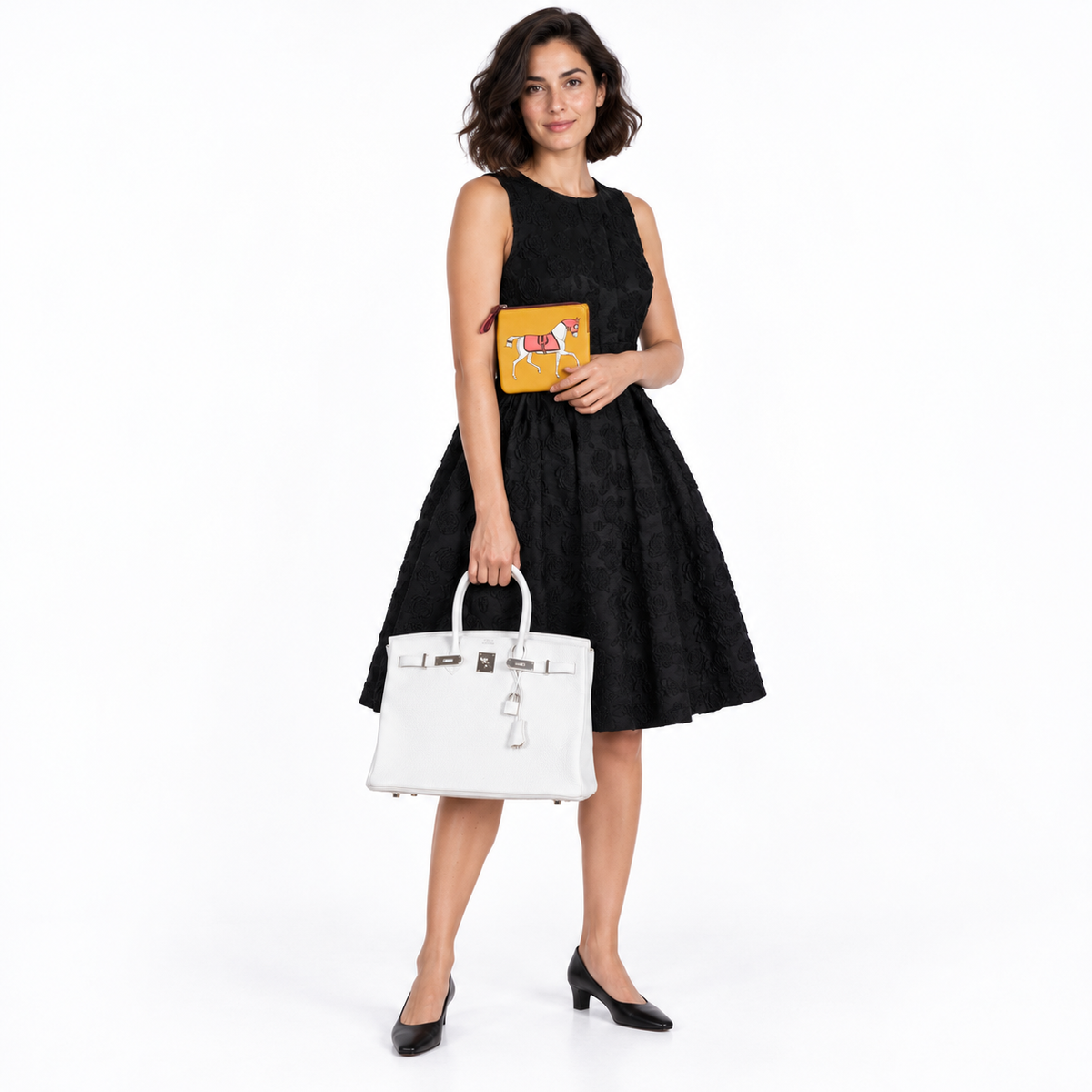Hermès Birkin 35 White Clemence with palladium hardware carried by a woman in a black dress holding a yellow horse pouch in a white studio