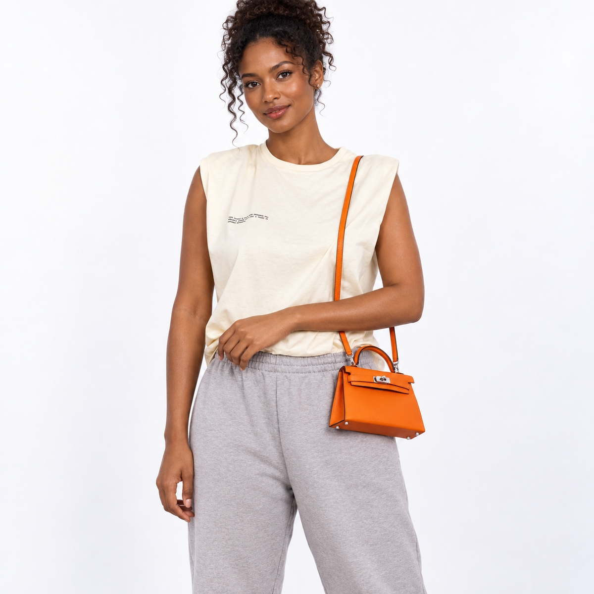 Hermès Kelly 20 Mini II Orange Chèvre with palladium hardware worn on the shoulder by an adult model in a white studio