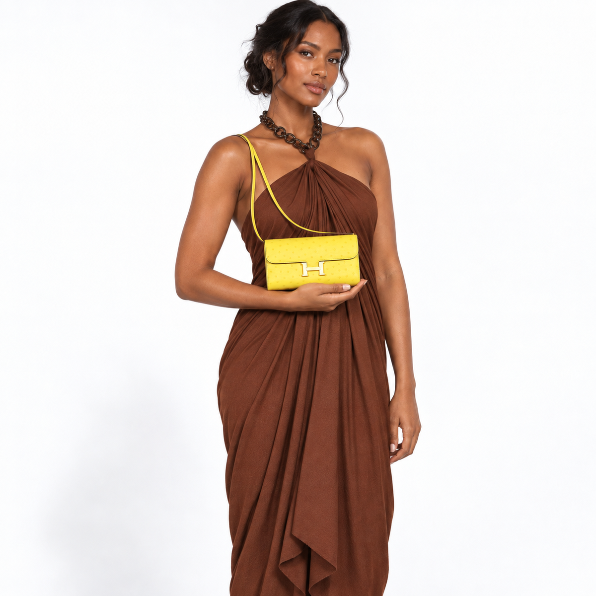 Hermès Constance Long To Go citron ostrich gold hardware held by a model on white