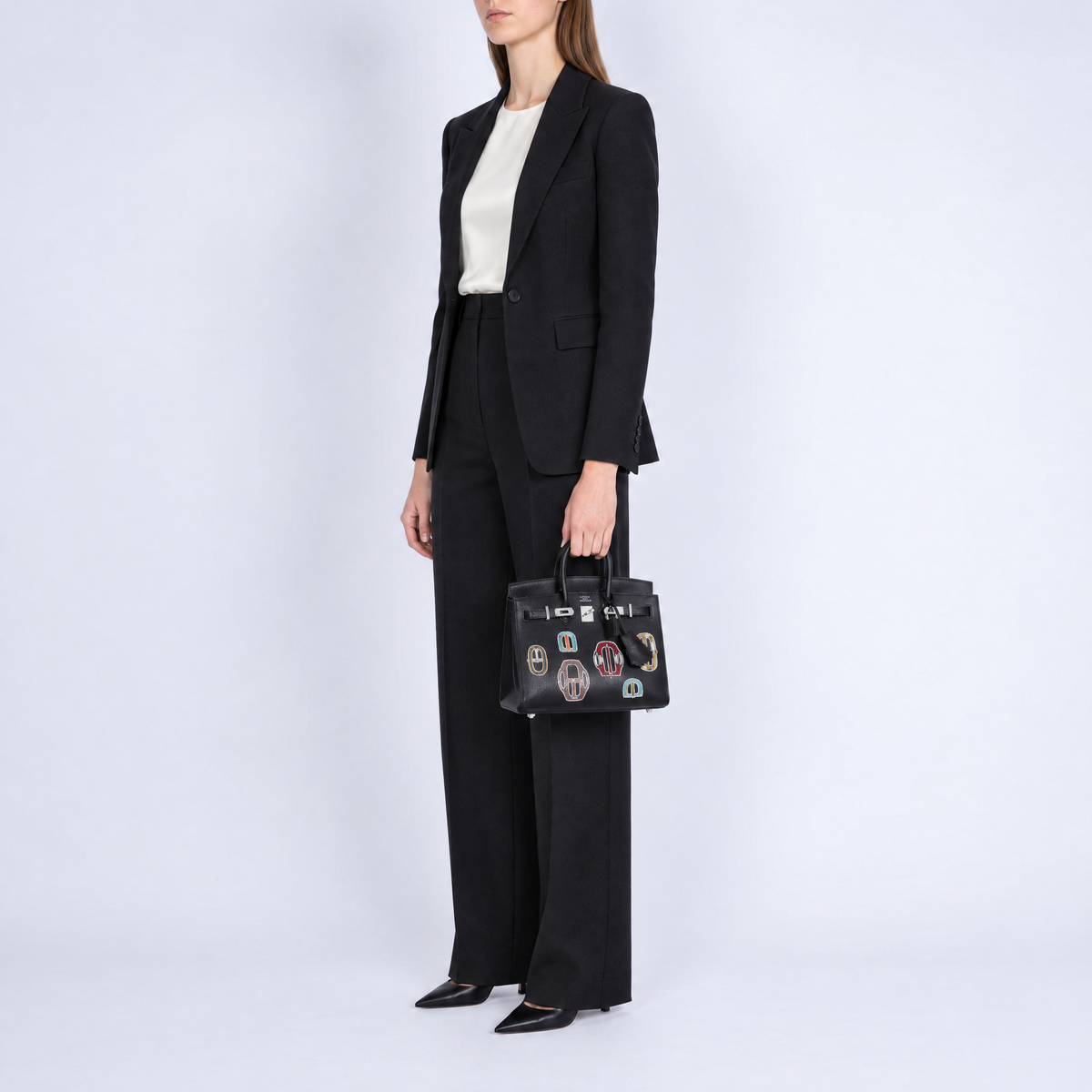Hermès Birkin 20 Bouclerie Moderne Casaque Noir with palladium hardware, carried by a model in tailored black suiting, three-quarter view.