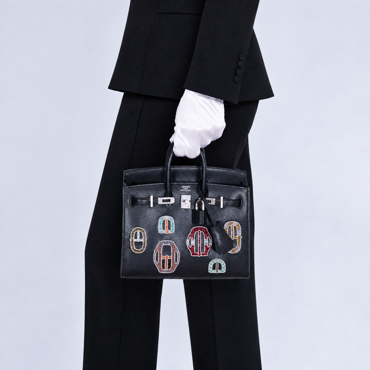 Close-up of Hermès Birkin 20 Bouclerie Moderne Casaque Noir beadwork and palladium hardware, held beside refined black tailoring.
