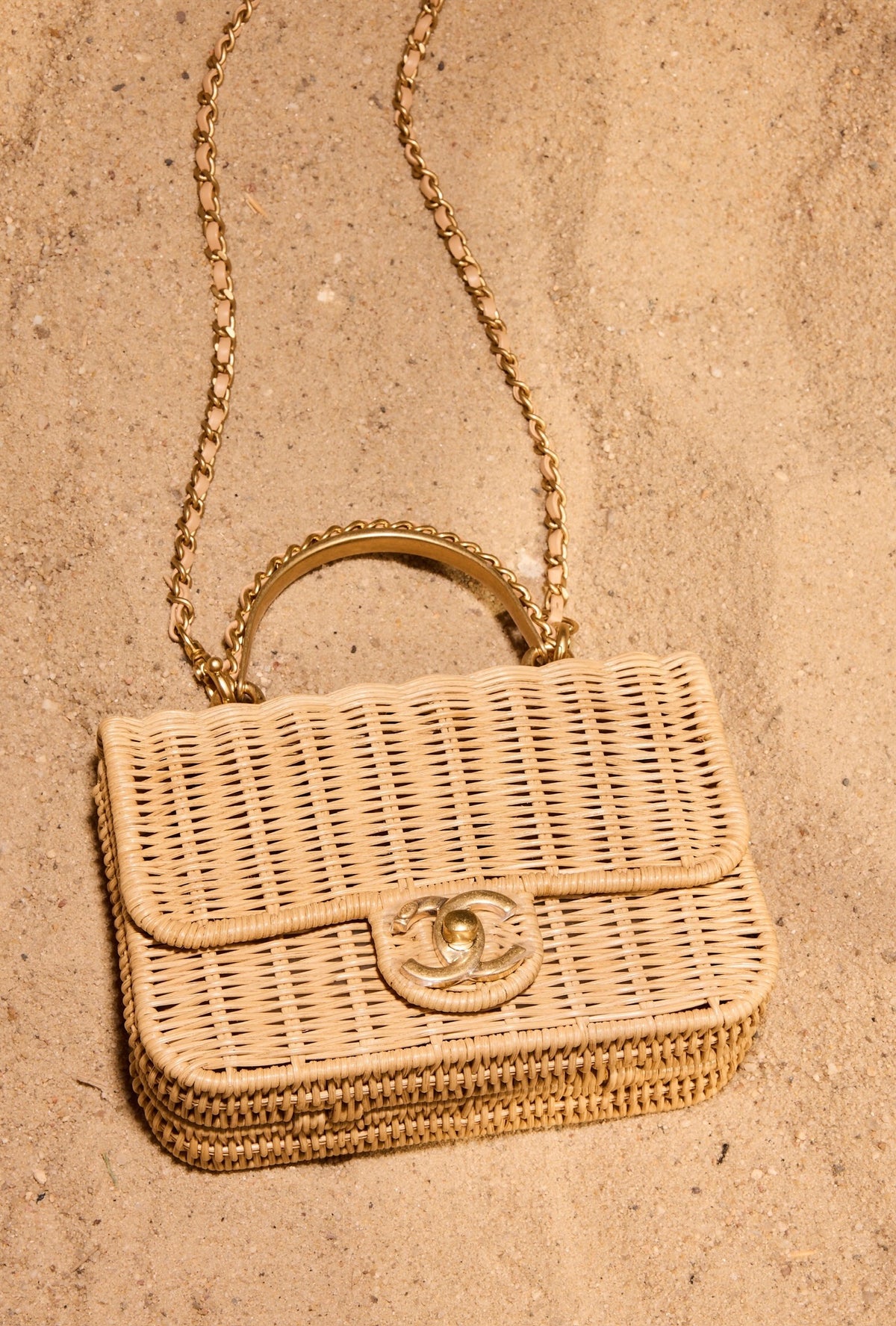 Chanel Mini Flap Bag with Top Handle Beige Braided Rattan Gold-Tone Hardware, lying on sand, close view