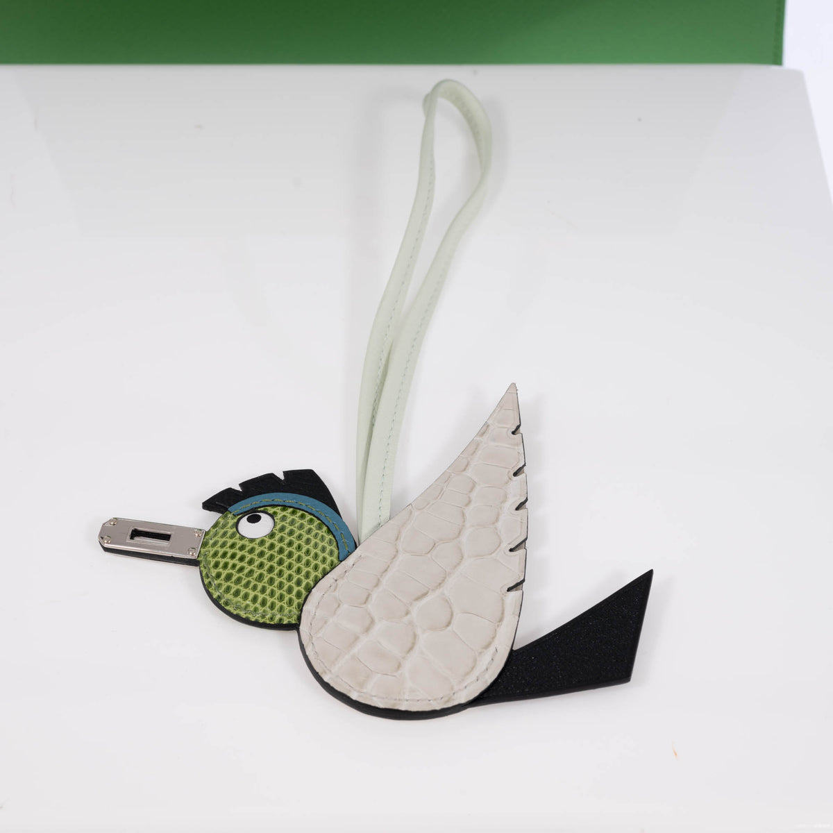 Hermès Birdy bag charm, opposite-side view showing the pale alligator wing, green lizard head, black leather tail and pale leather loop.