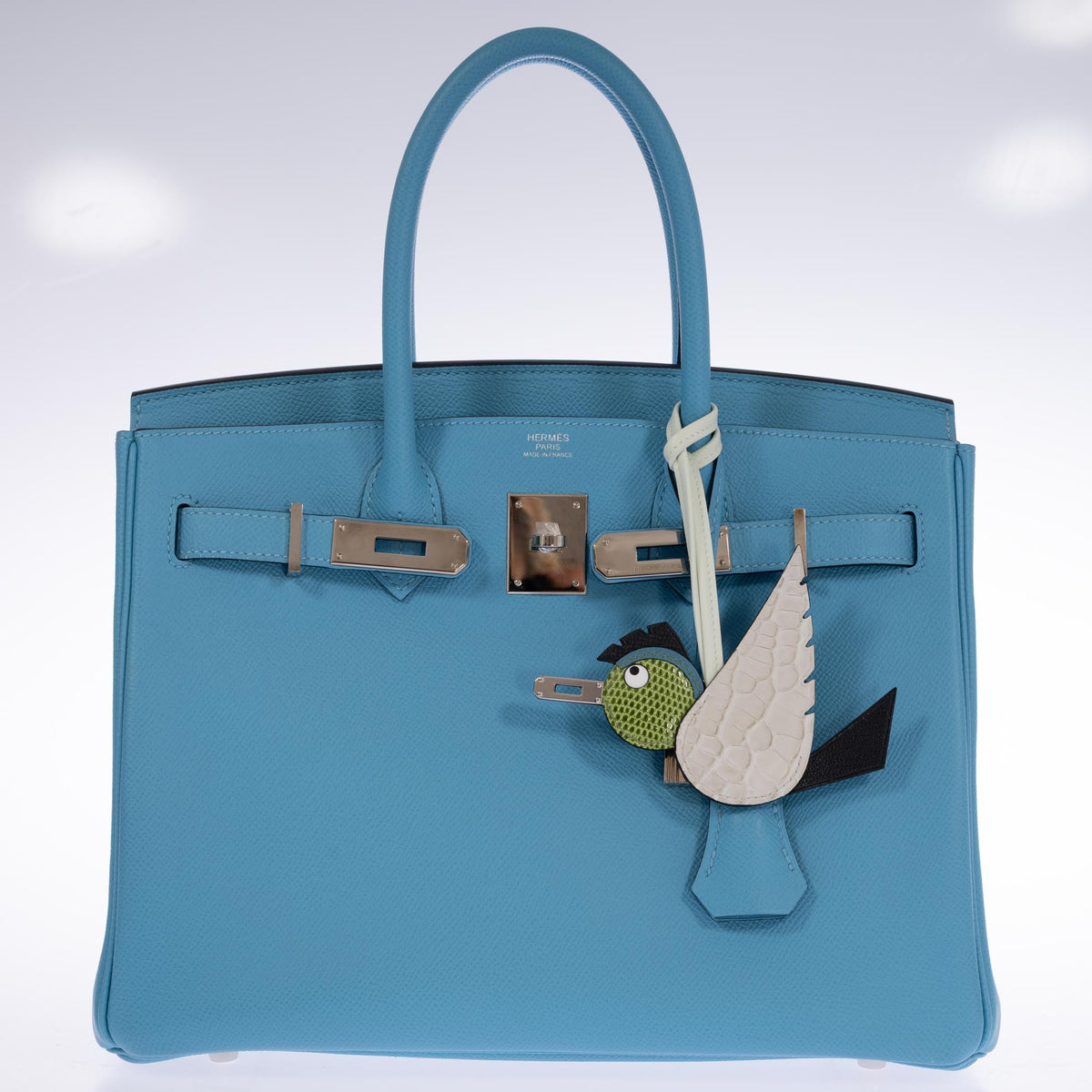 Hermès Birdy bag charm with a Béton alligator wing and Pelouse lizard head, attached to a blue Birkin with palladium hardware, which is sold separately.