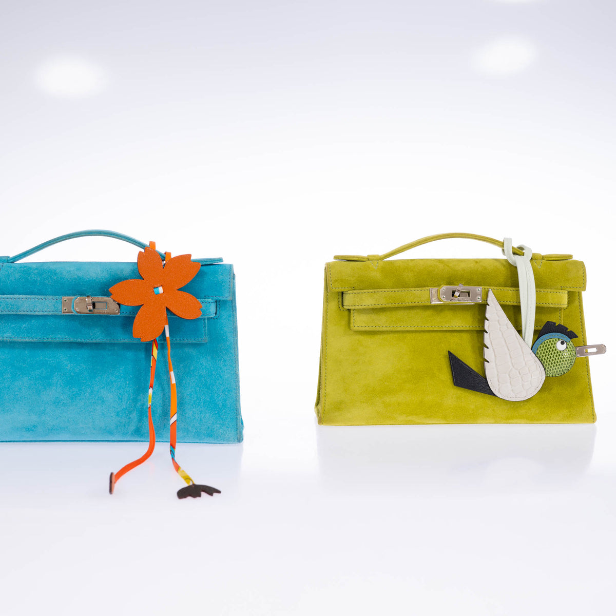 Hermès Birdy bag charm in Béton, Noir and Pelouse on a yellow-green Kelly Pochette, beside a turquoise Kelly Pochette with an orange flower charm, all sold separately.