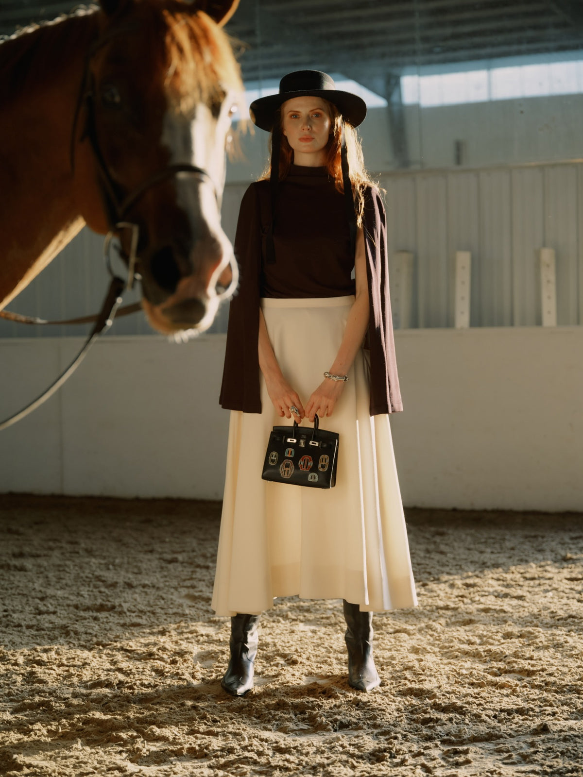 Hermès Birkin 20 Sellier Bouclerie Moderne Casaque Noir Chèvre Chamkila Palladium Hardware, carried by a model in a riding arena beside a horse