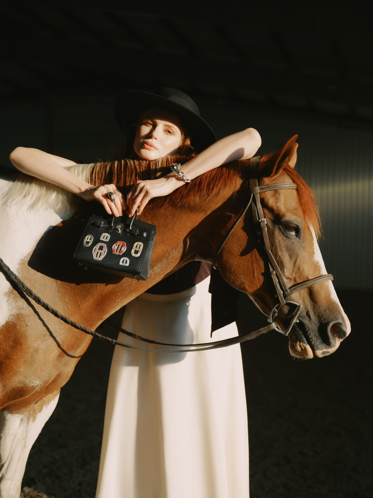 Hermès Birkin 20 Sellier Bouclerie Moderne Casaque Noir Chèvre Chamkila Palladium Hardware, held by a model leaning over a horse's neck
