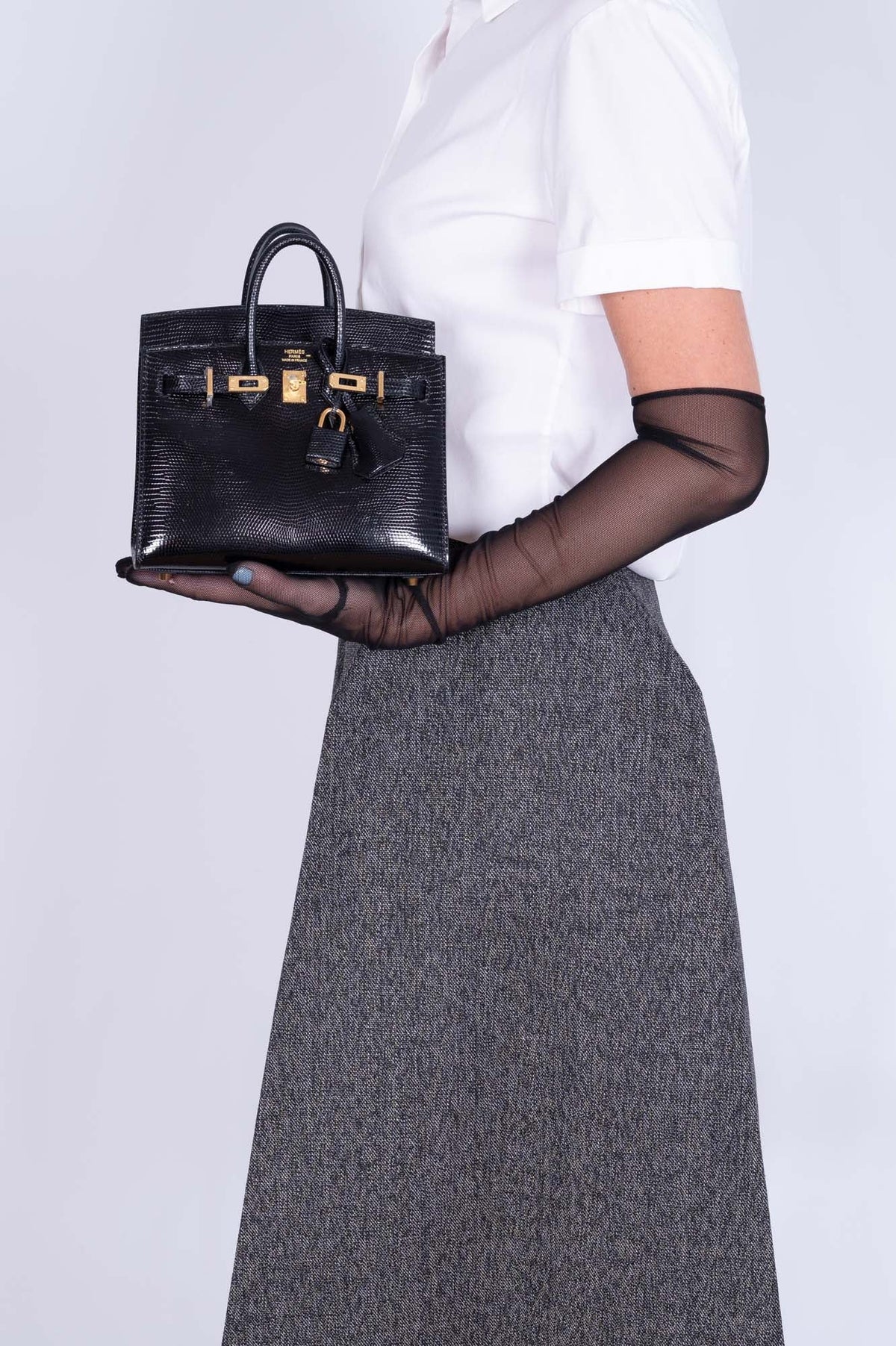 Hermès Birkin 20 Sellier Noir Shiny Varanus Niloticus Lizard Gold Hardware, held in the palm of a model
