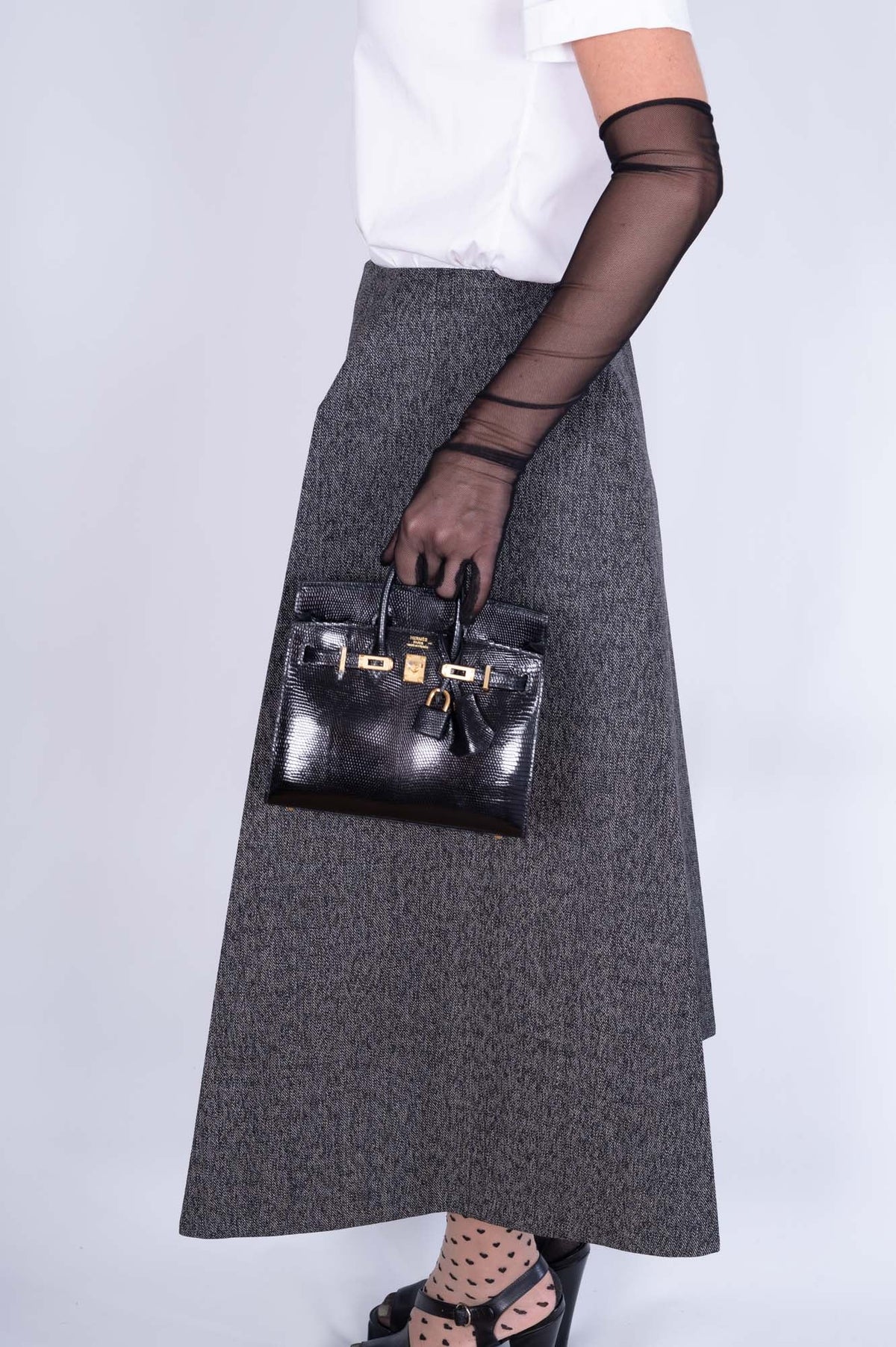 Hermès Birkin 20 Sellier Noir Shiny Varanus Niloticus Lizard Gold Hardware, carried by hand by a model, side view