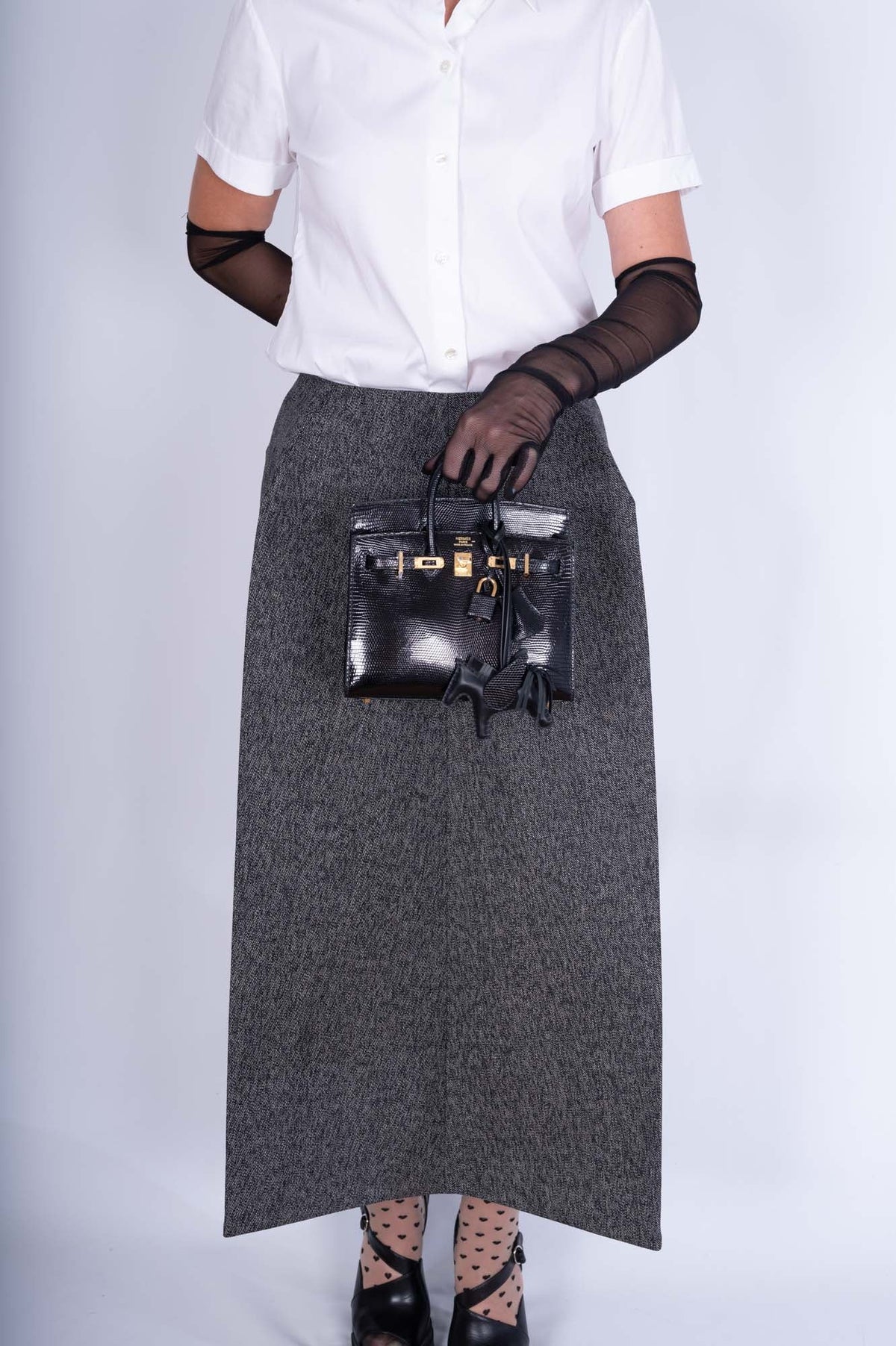 Hermès Birkin 20 Sellier Noir Shiny Varanus Niloticus Lizard Gold Hardware, carried by hand by a model, styled with a Rodeo charm, not included