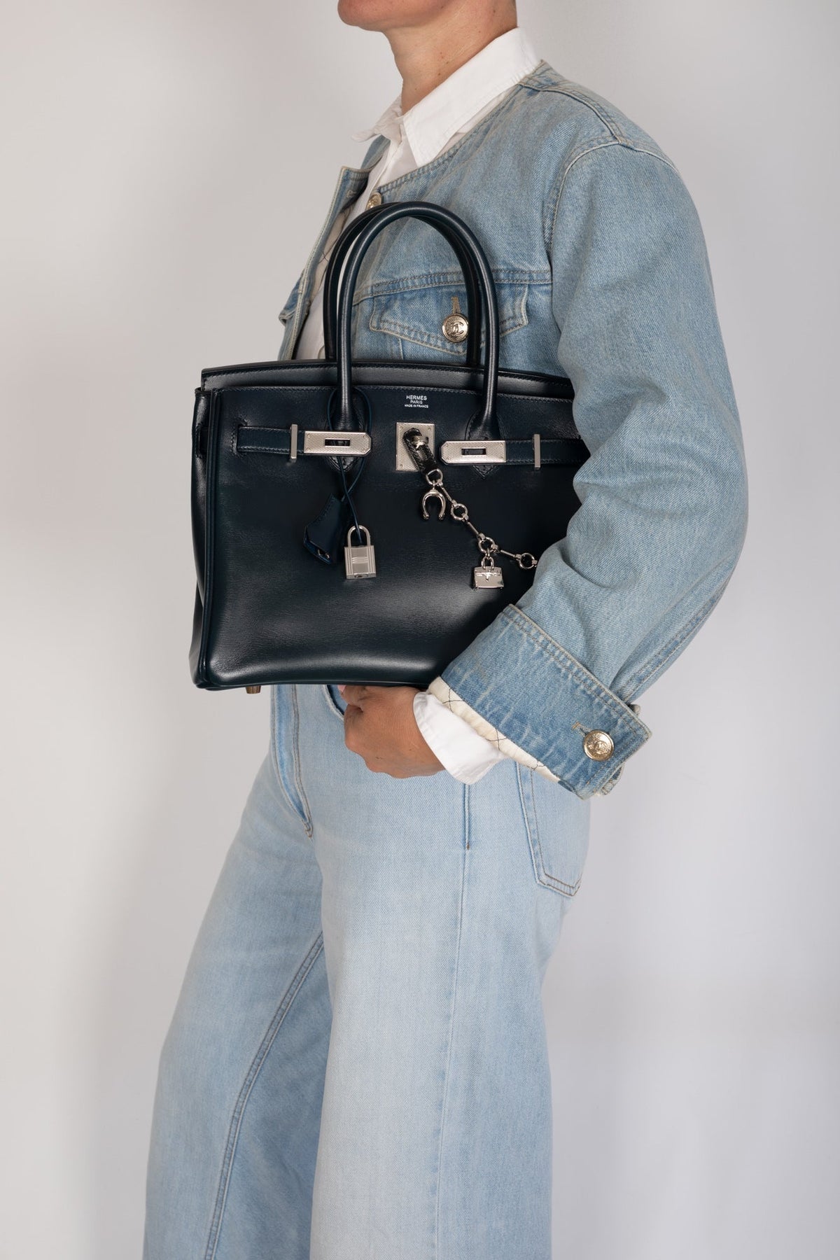 Hermès Birkin 30 Bleu de Prusse Box Calf Guilloche Palladium Hardware, held under the arm with the flap open, styled with a charm chain, sold separately