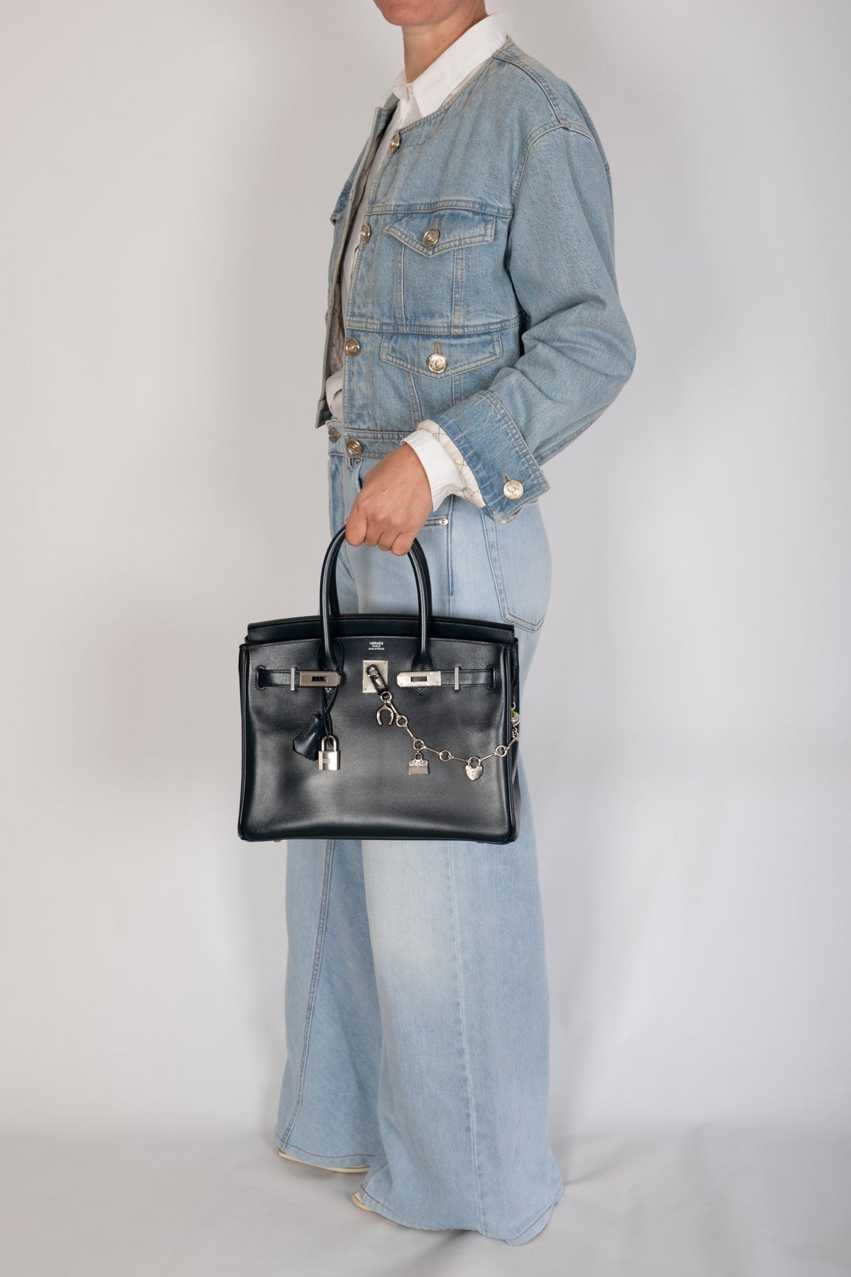 Hermès Birkin 30 Bleu de Prusse Box Calf Guilloche Palladium Hardware, carried by the handles in a full-length view showing scale, styled with a charm chain, sold separately