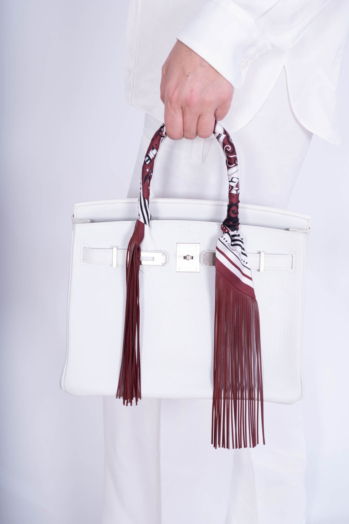 Hermès Birkin 30 HSS Blanc Clémence Brushed Palladium Hardware, carried by its handle by a model, shown with a fringed twilly that is not included