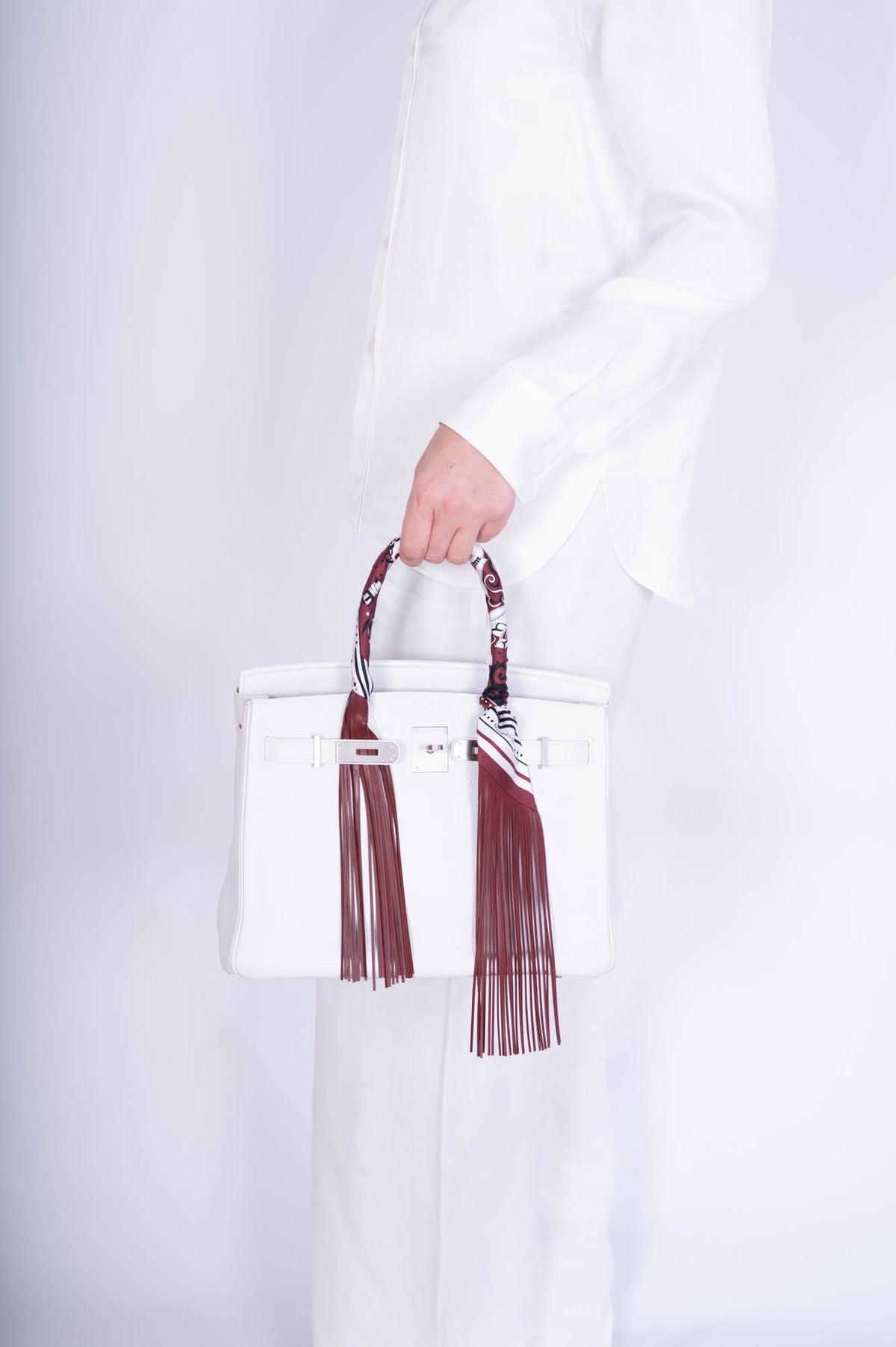Hermès Birkin 30 HSS White Clemence Brushed Palladium Hardware, carried by its handle by a model, side view, shown with a fringed twilly that is not included
