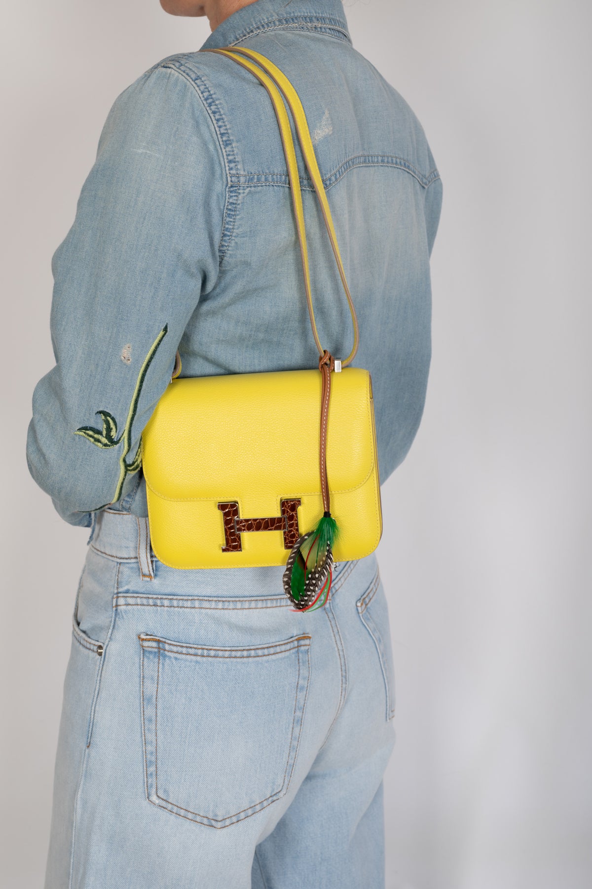 Hermès Constance 18 Mini Lime Evergrain Miel Alligator Buckle Palladium Hardware, worn on the shoulder by a model, shown with a charm that is not included