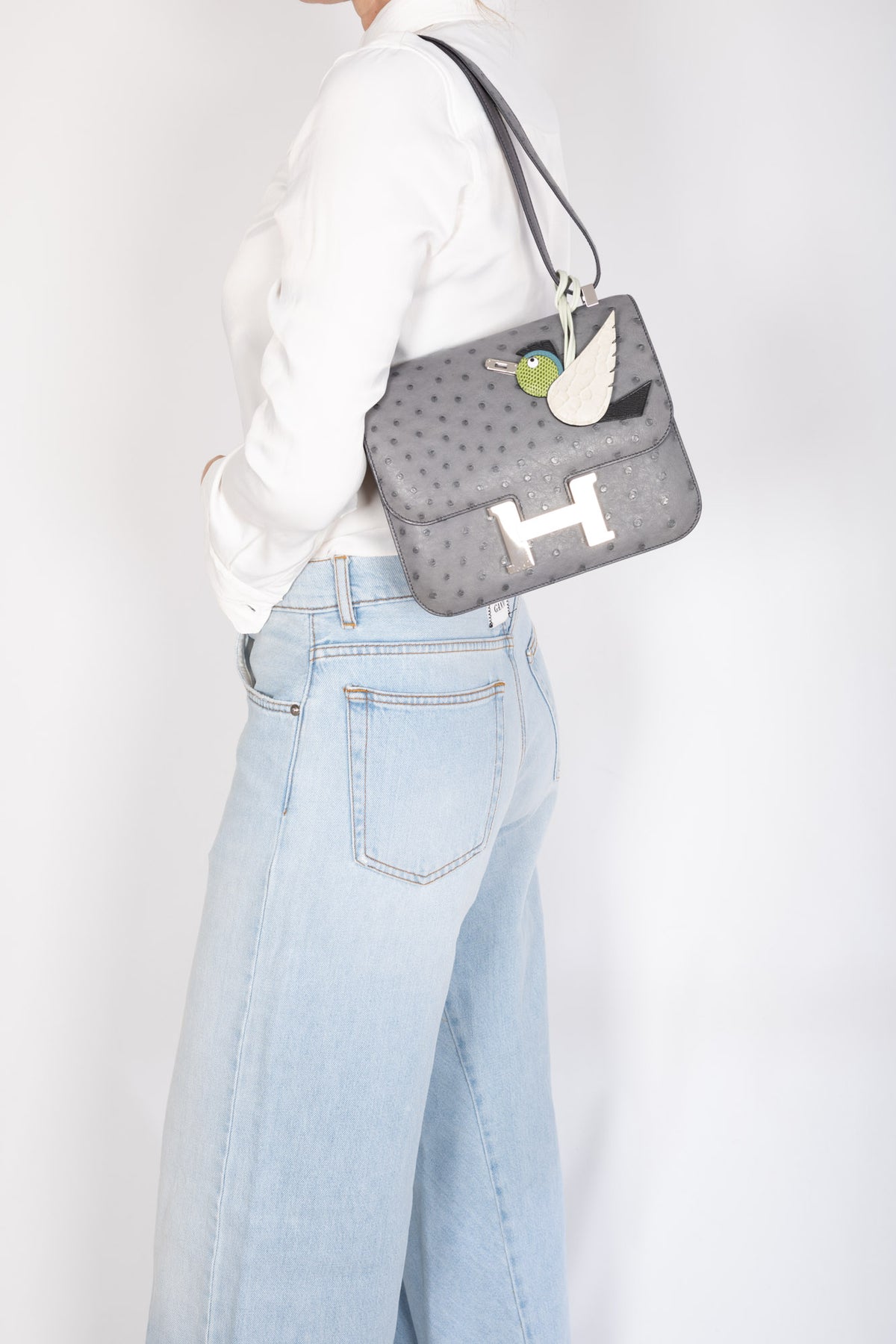 Hermès Constance III 24 Gris Agate Ostrich Palladium Hardware, worn on the shoulder by a model, close view, styled with a charm, sold separately