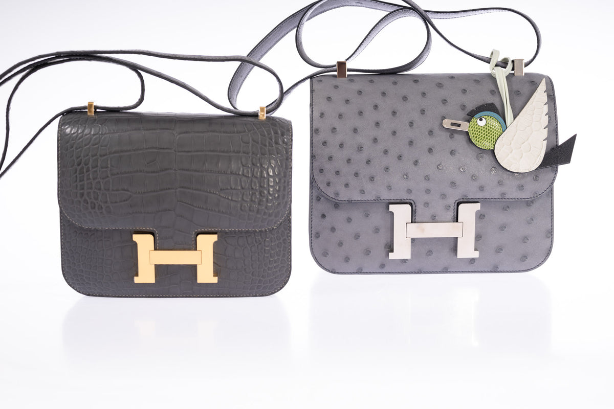 Hermès Constance III 24 Gris Agate Ostrich Palladium Hardware, beside a Constance 18 in Graphite alligator, styled with a charm, both sold separately