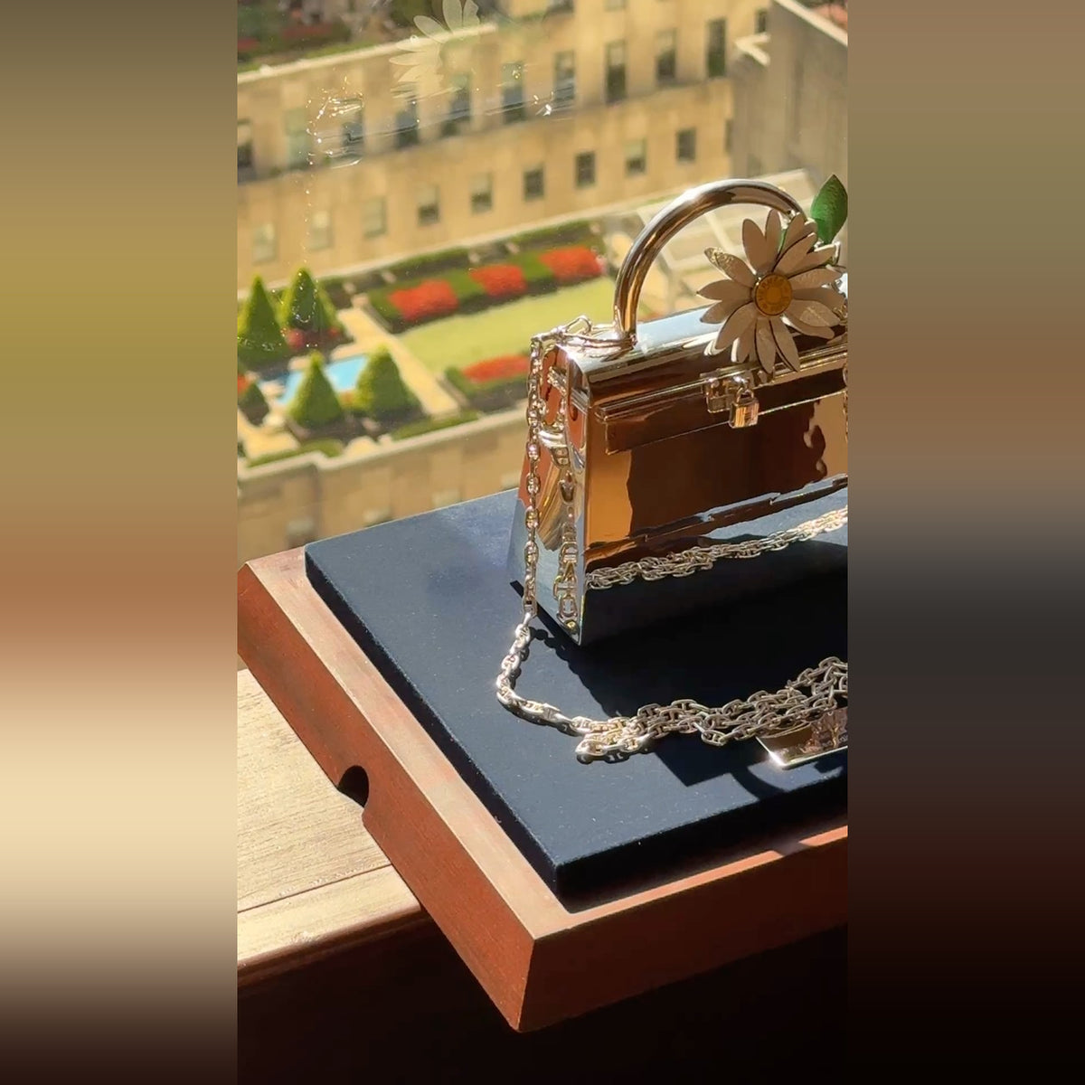 Hermès Kelly 15 Sterling Silver Chaîne d'Ancre Strap, on its stand by a window, shown with a marguerite charm, charm sold separately