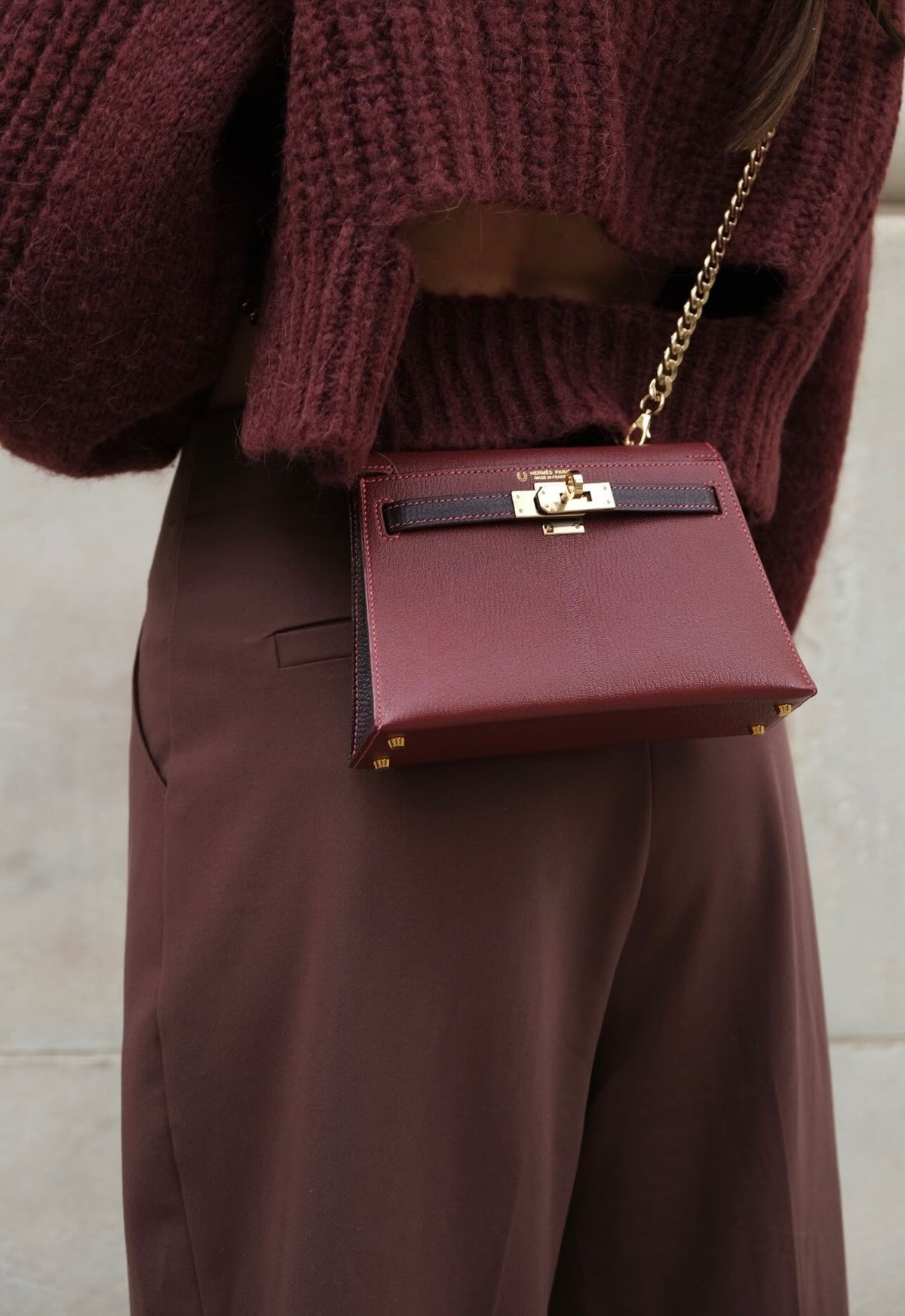Hermès Kelly 20 Mini II HSS Multico Bordeaux and Raisin Chèvre Gold Hardware, worn crossbody on a chain by a model