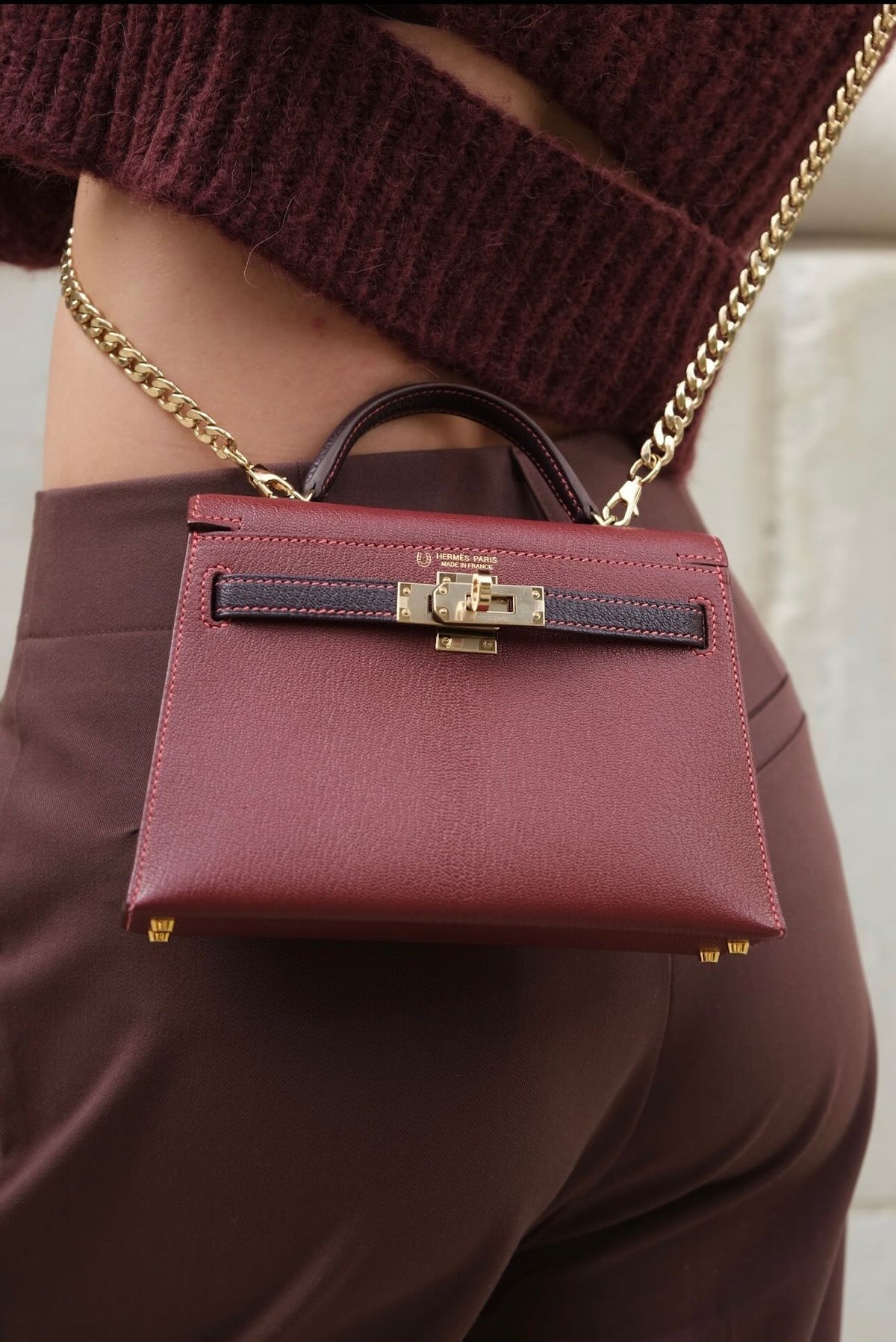 Hermès Kelly 20 Mini II HSS Multico Bordeaux and Raisin Chèvre Gold Hardware, worn on a chain by a model, close view