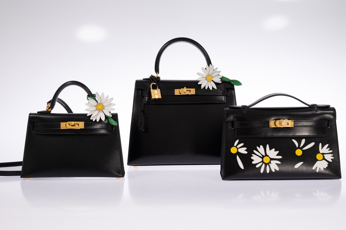 Hermès Kelly 20 Mini II Sellier in Noir Box calf with gold hardware at left, beside a Kelly 25 and decorated Kelly Pochette; daisy charms and other bags sold separately.