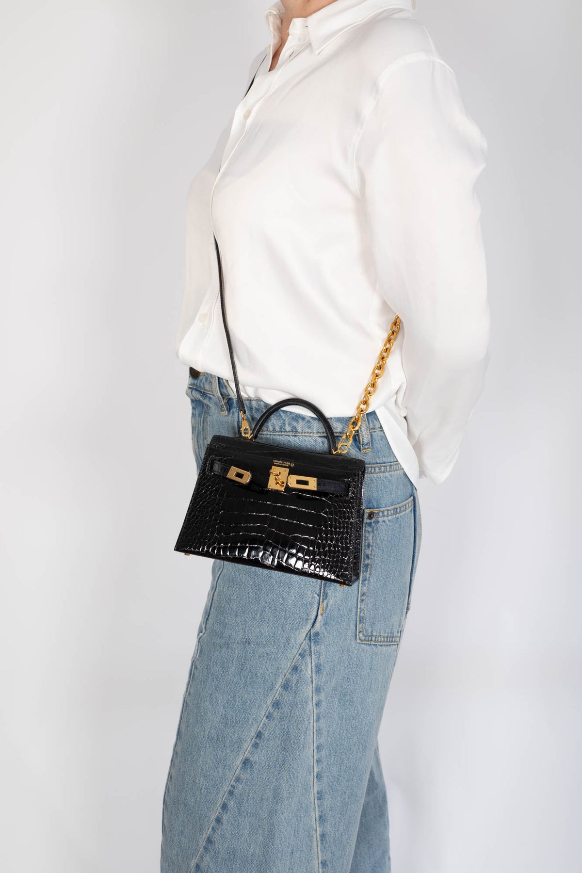 Hermès Kelly 20 Mini II Sellier Noir Shiny Alligator Gold Hardware, worn crossbody by a model on a chain, sold separately