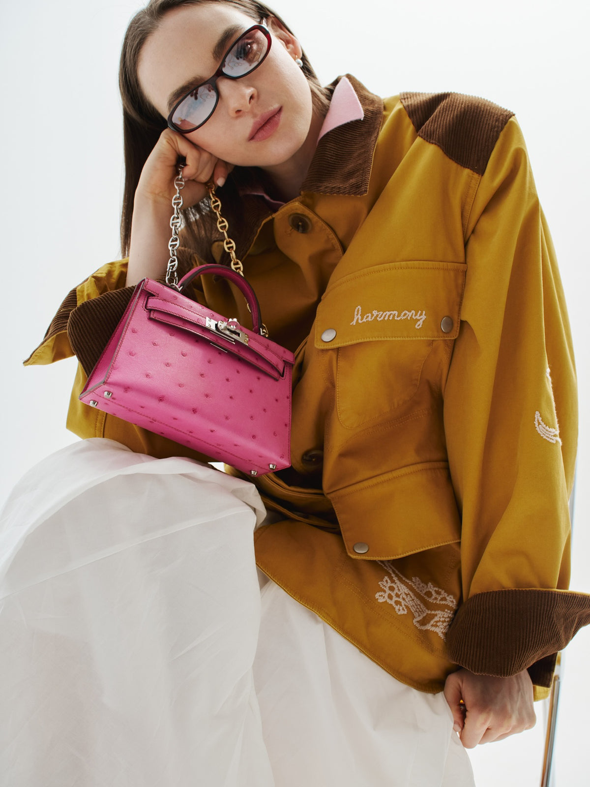 Hermès Kelly 20 Mini II Sellier Rose Tyrien Ostrich Palladium Hardware, carried on a chain by a seated model