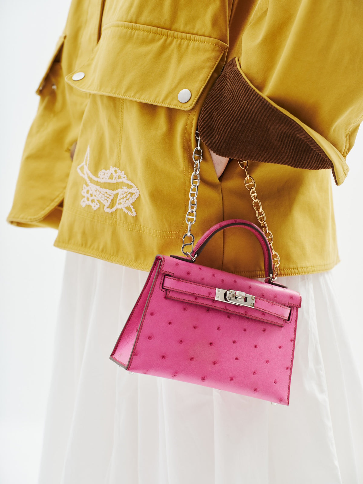 Hermès Kelly 20 Mini II Sellier Rose Tyrien Ostrich Palladium Hardware, carried on a chain by a model, close view