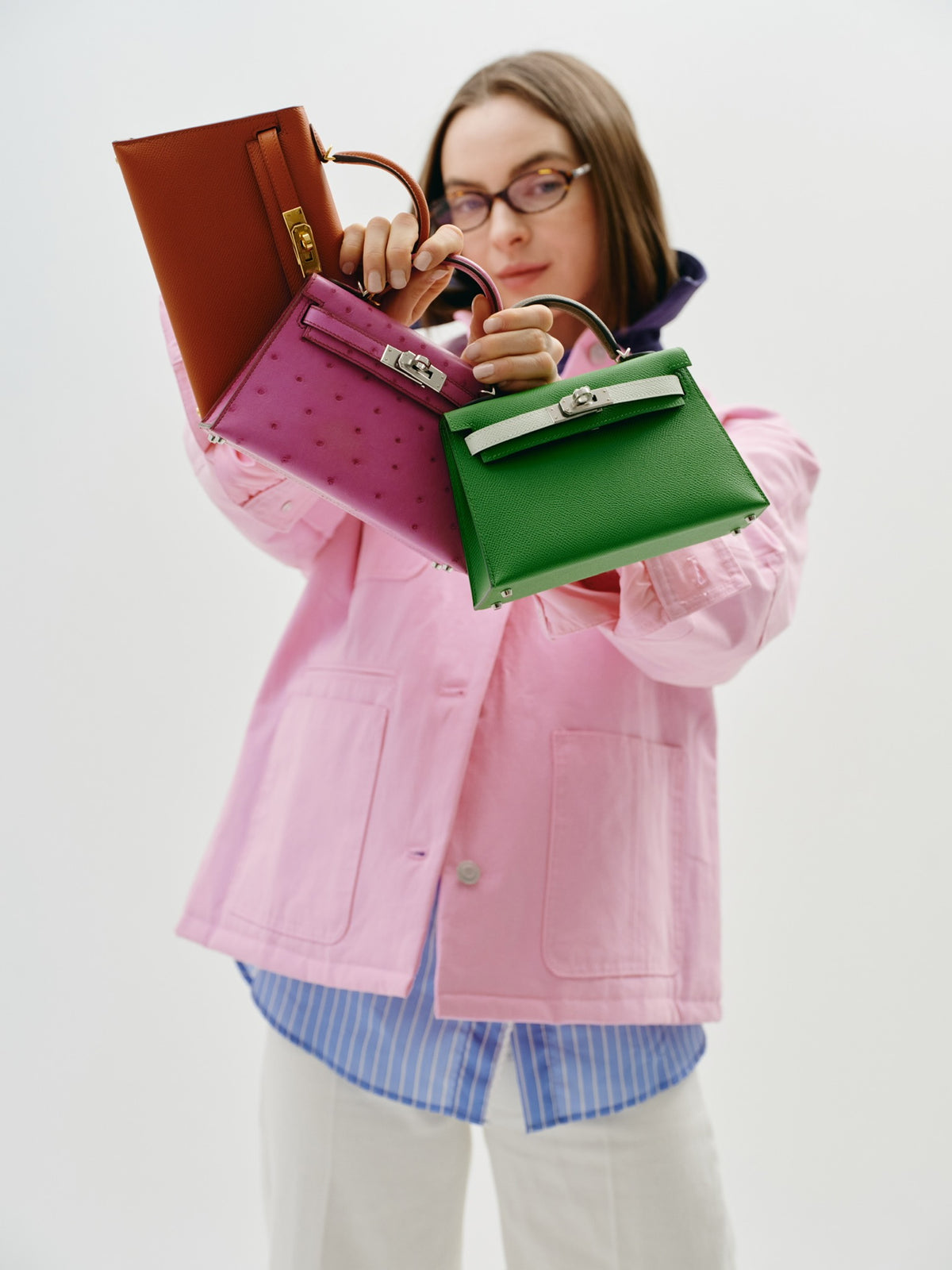 Hermès Kelly 20 Mini II Sellier Rose Tyrien Ostrich Palladium Hardware, held by a model with two other Kelly Mini bags, sold separately