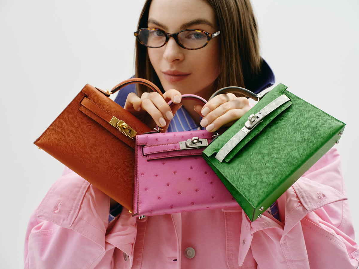 Hermès Kelly 20 Mini II Sellier Rose Tyrien Ostrich Palladium Hardware, held up by a model with two other Kelly Mini bags, sold separately