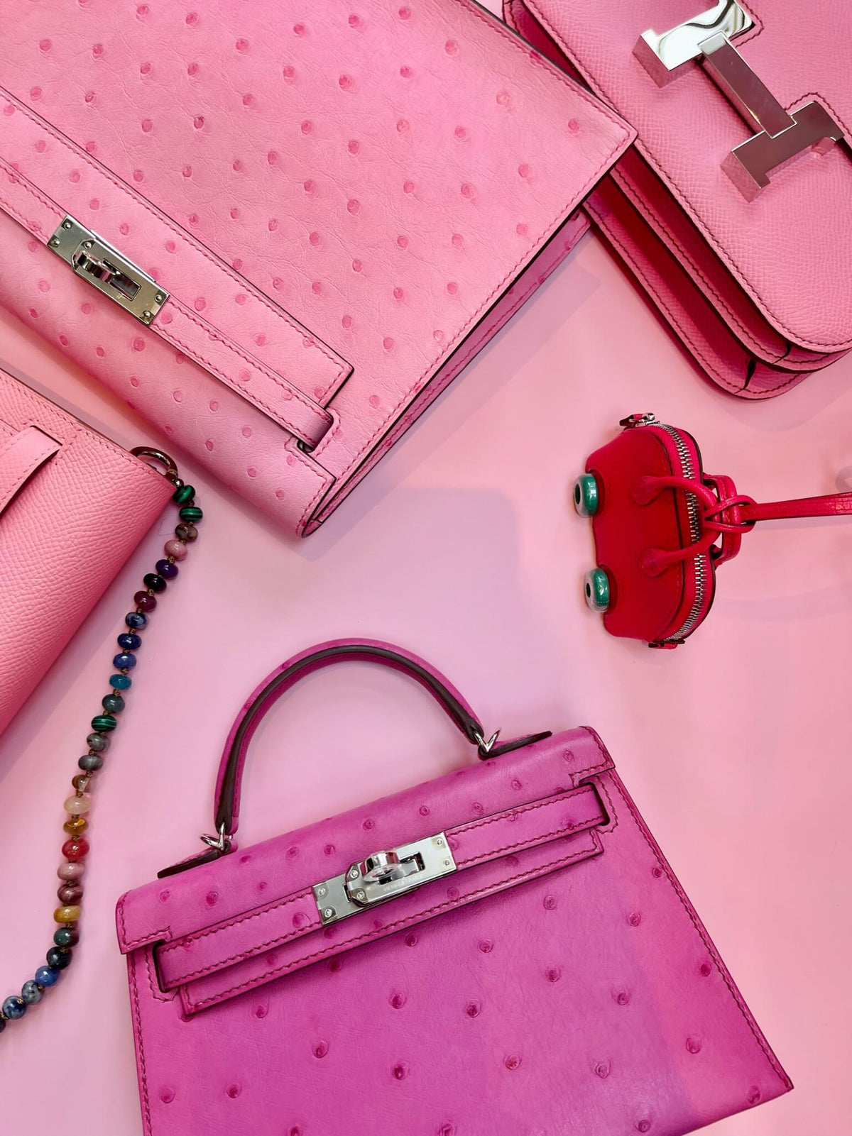 Hermès Kelly 20 Mini II Sellier Rose Tyrien Ostrich Palladium Hardware, flat lay with other pink pieces, a beaded strap and a charm