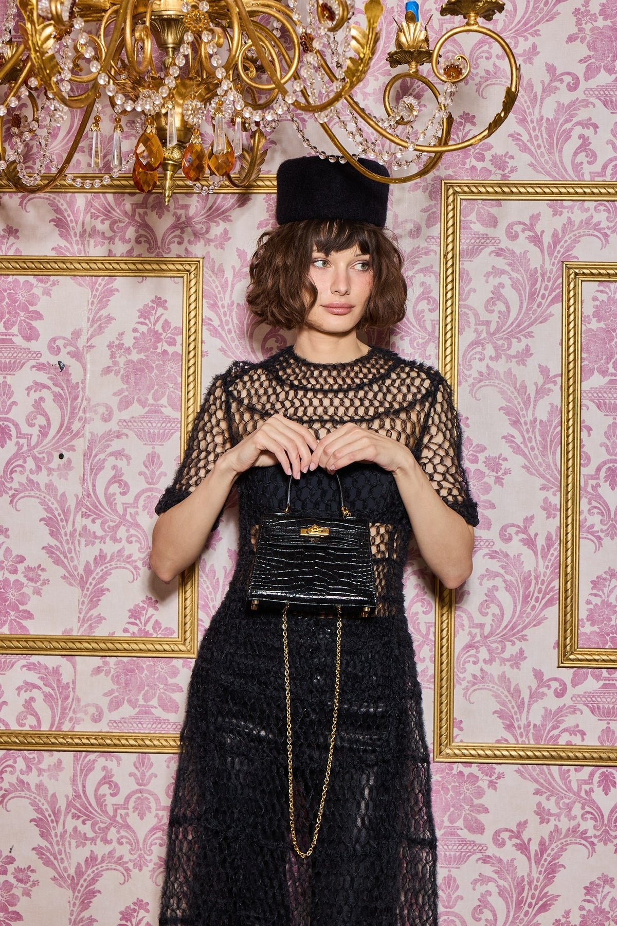 Hermès Kelly 20 Vintage Retourne Noir Shiny Porosus Crocodile Gold Hardware, held at the waist by a model, with a chain strap