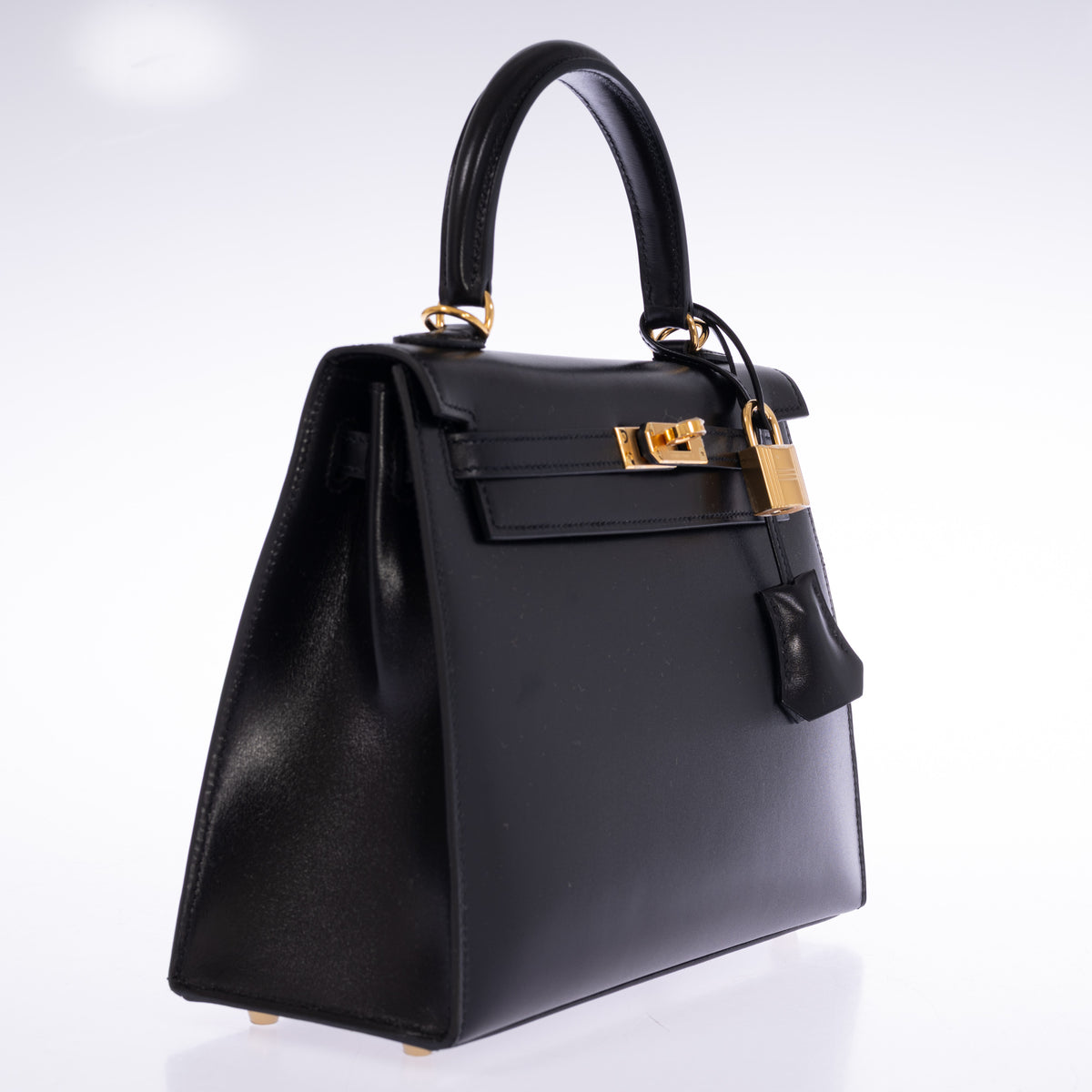 Hermès Kelly 25 Sellier in Noir Box calf with gold hardware, three-quarter view showing the side gusset, external stitching and clochette.