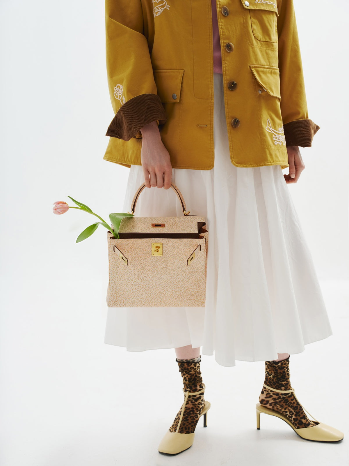 Hermès Kelly 28 Retourne Orange Dalmatian Buffalo Skipper Gold Hardware, carried by a model, with a tulip tucked inside
