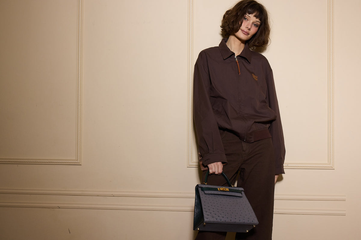 Hermès Kelly 28 Sellier HSS Gris Agate/Vert Titien Ostrich Brushed Gold Hardware, carried by a model leaning on a wall