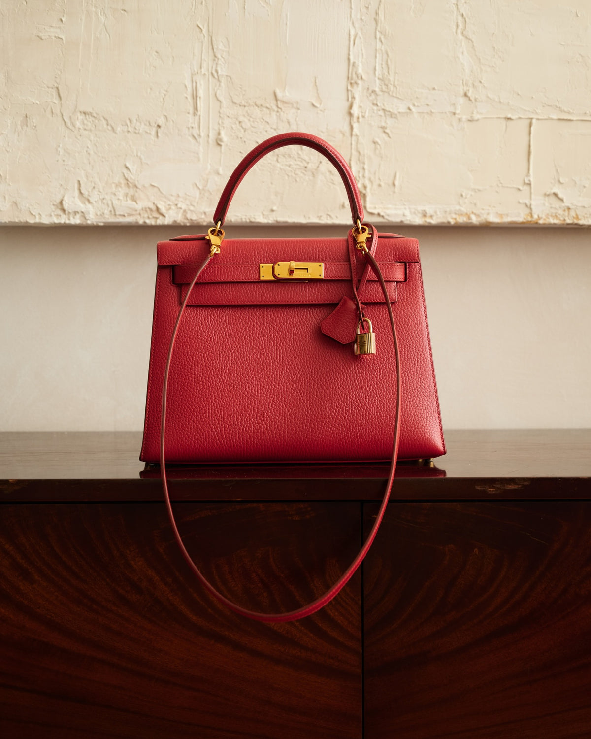 Hermès Kelly 28 Sellier Rouge Vif Ardennes Gold Hardware, standing on a sideboard with its shoulder strap