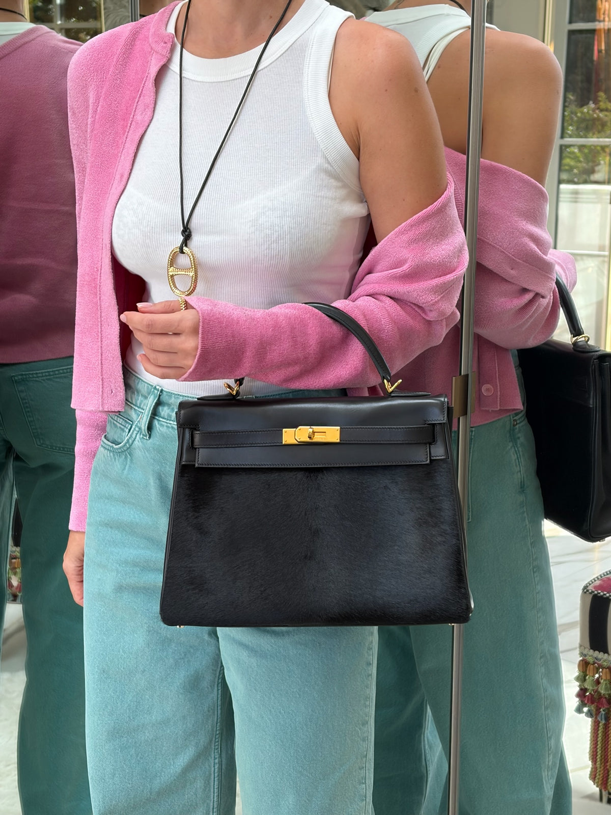 Hermès Kelly 32 Noir Box leather and pony skin with Gold hardware, carried on the forearm with a pink cardigan and jeans.