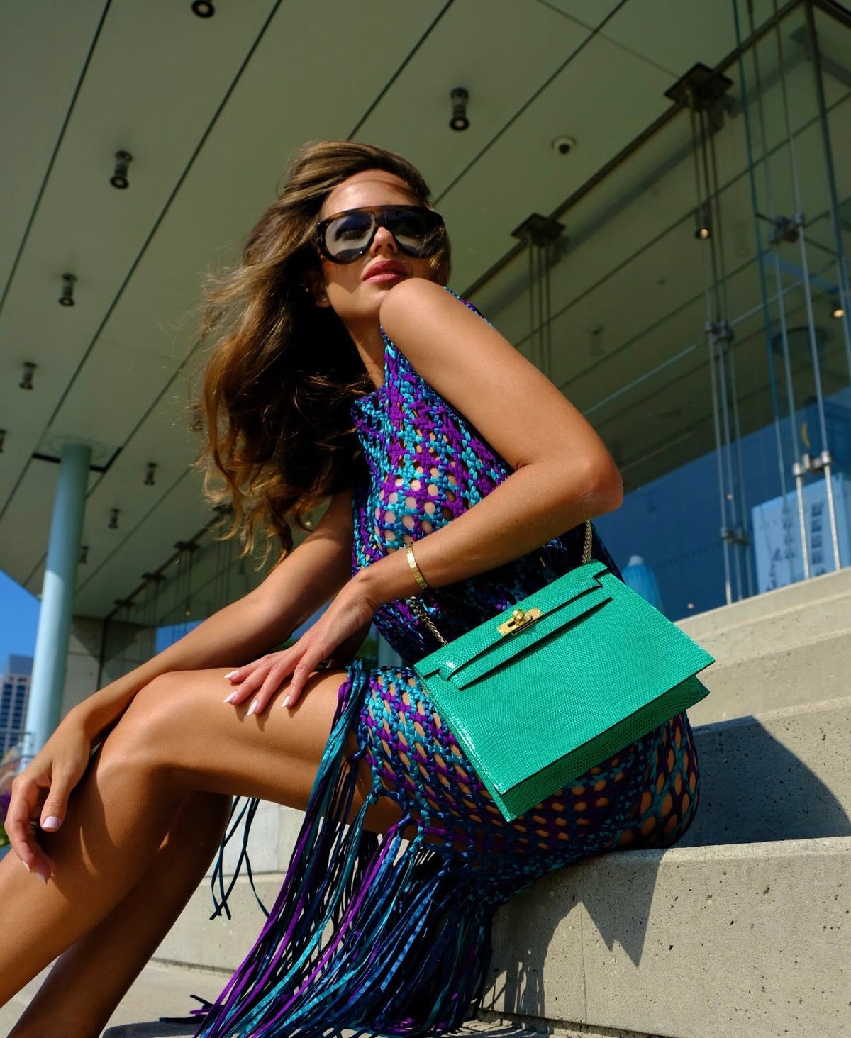 Hermès Kelly Danse II Menthe Shiny Nilo Lizard Gold Hardware, worn on a chain by a model seated on steps