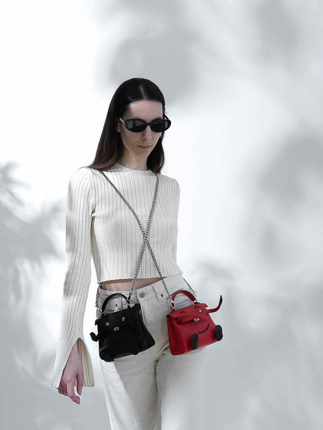 Hermès Kelly Doll Quelle Idole Noir Gulliver Palladium Hardware, worn crossbody on a chain by a model with a red Kelly Doll