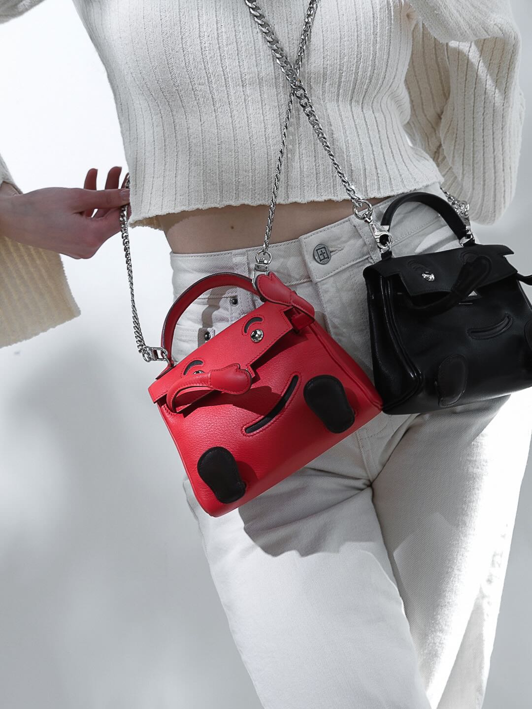 Hermès Kelly Doll Quelle Idole Noir Gulliver Palladium Hardware, worn on a chain by a model with a red Kelly Doll, close view
